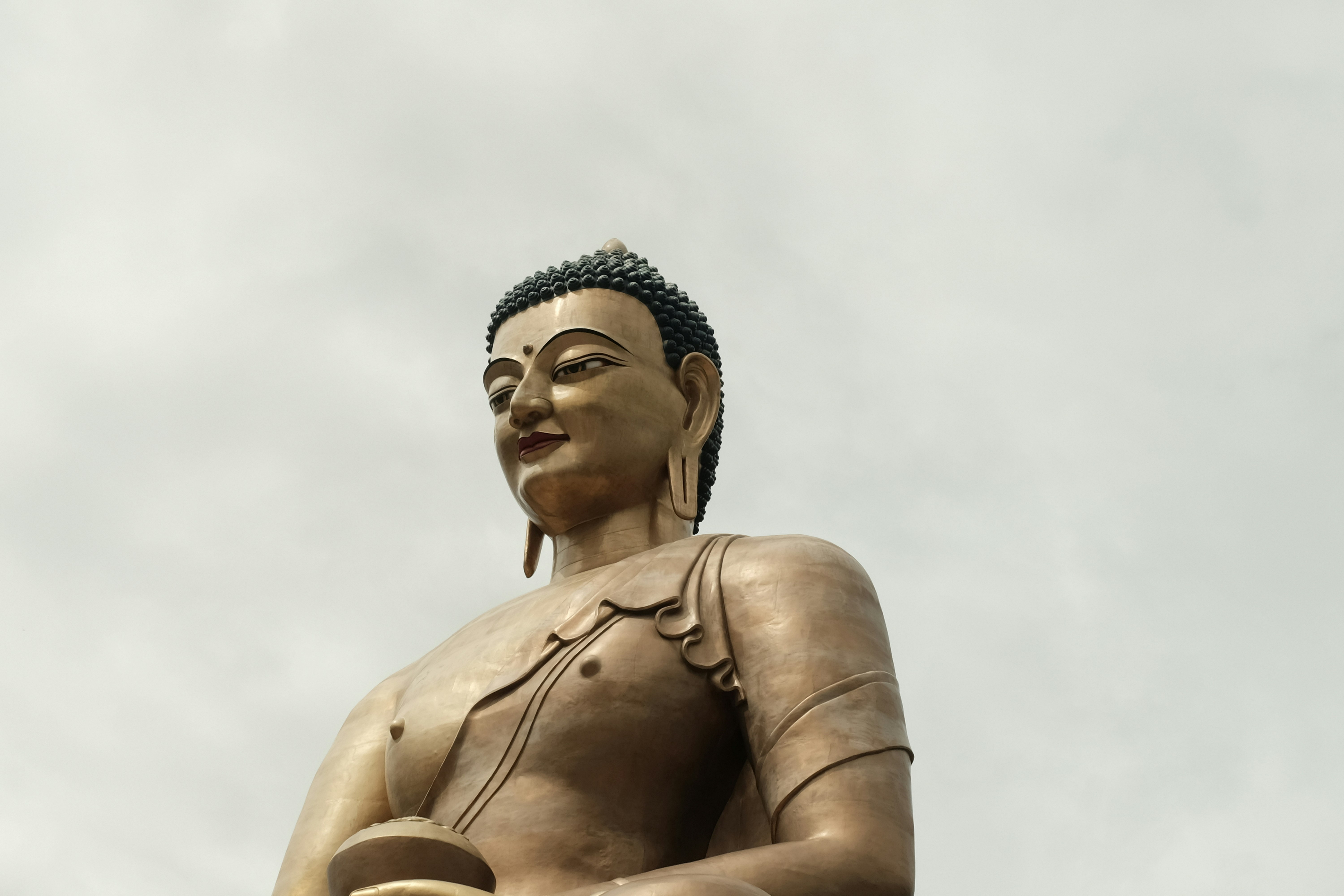 A golden buddha statue smiles against the cloudy sky.