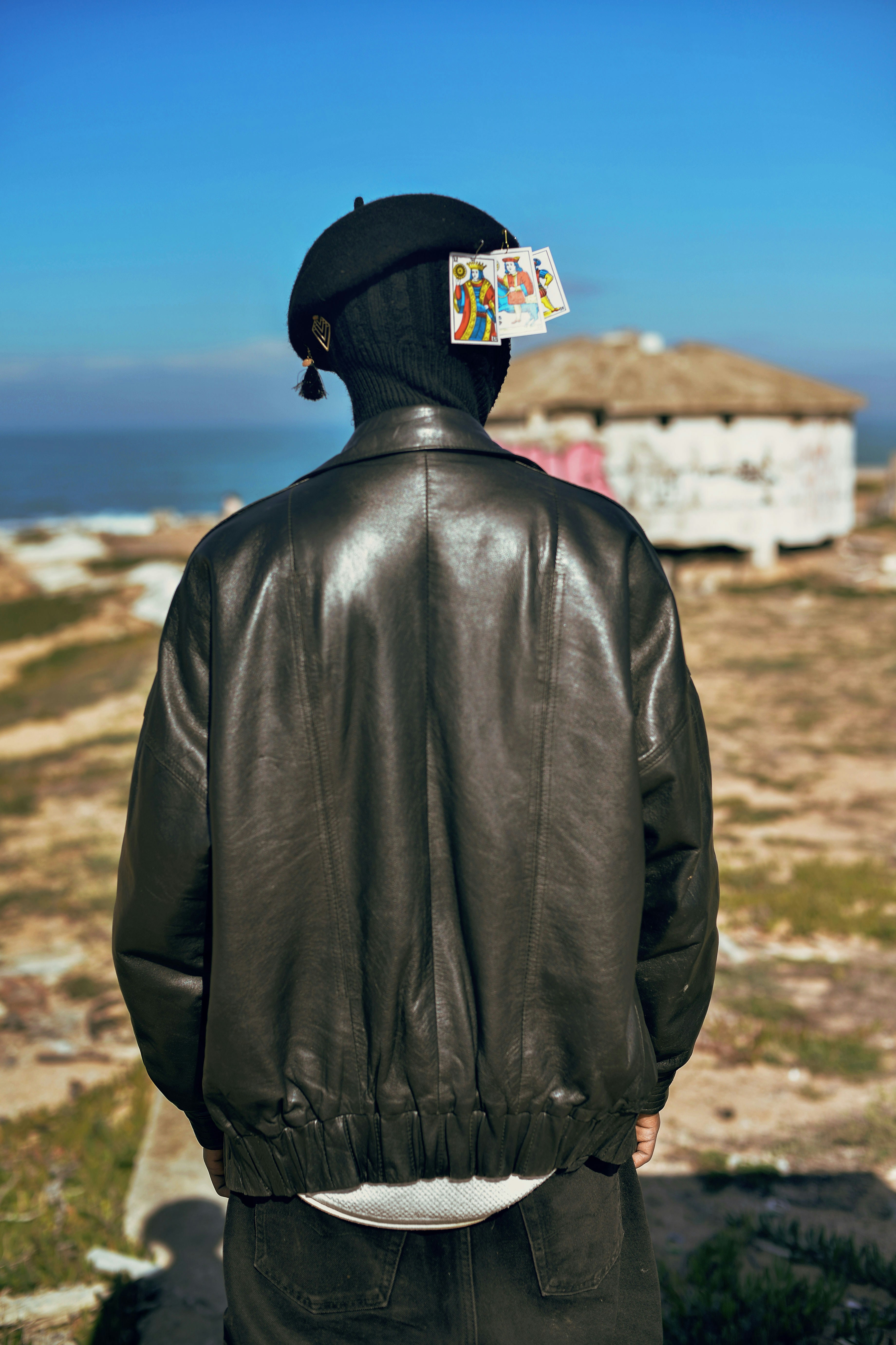 Person in black jacket stands before a coastal scene.
