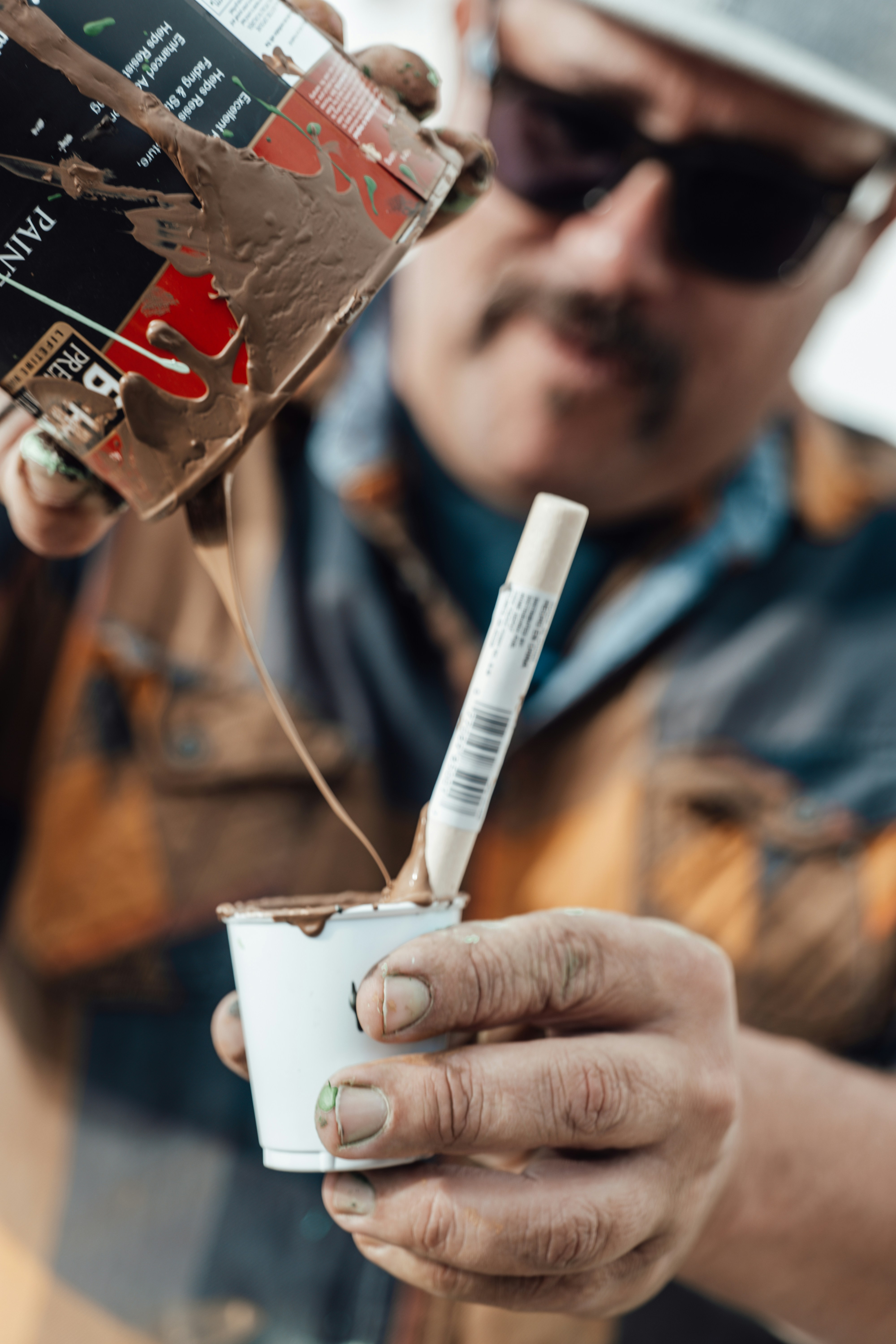 A person pouring brown paint from a metal can into a cup.