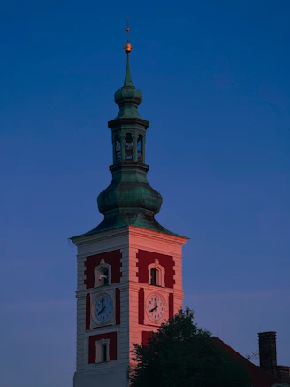 A clock tower glows at dusk under a blue sky.