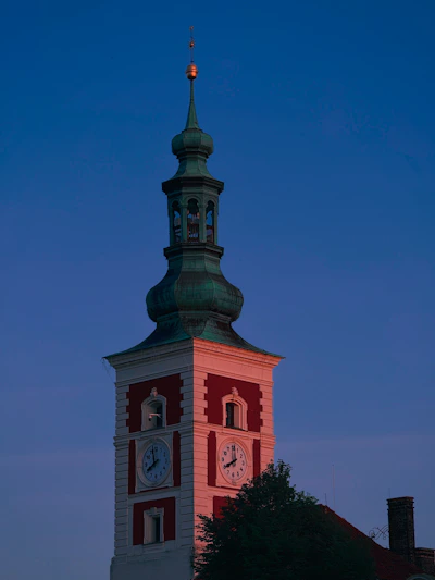 A clock tower glows at dusk under a blue sky.