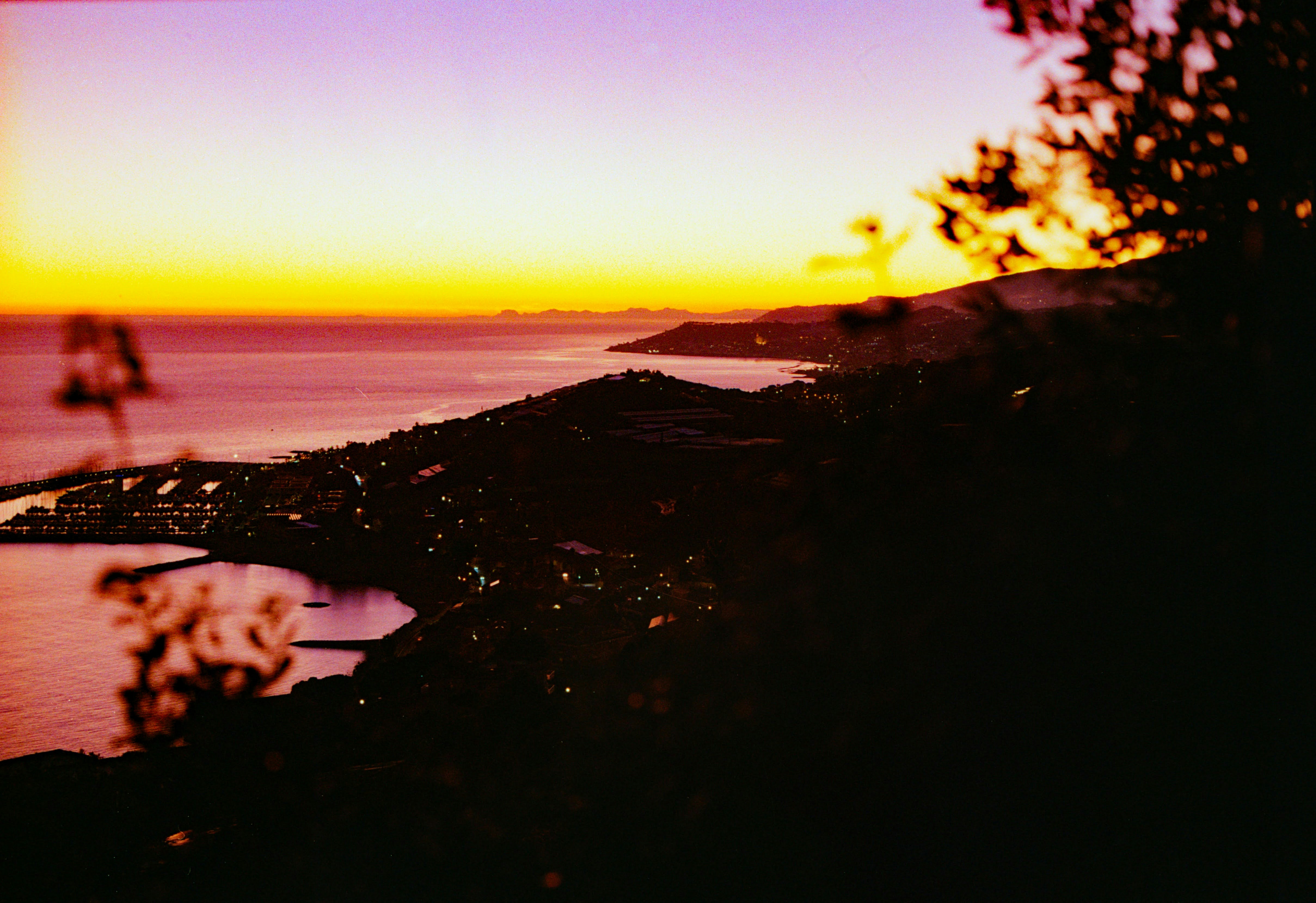 Sunset over the ocean with city lights.