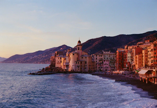 Tall coloured houses and a church on the seafront of a Ligurian town at dusk