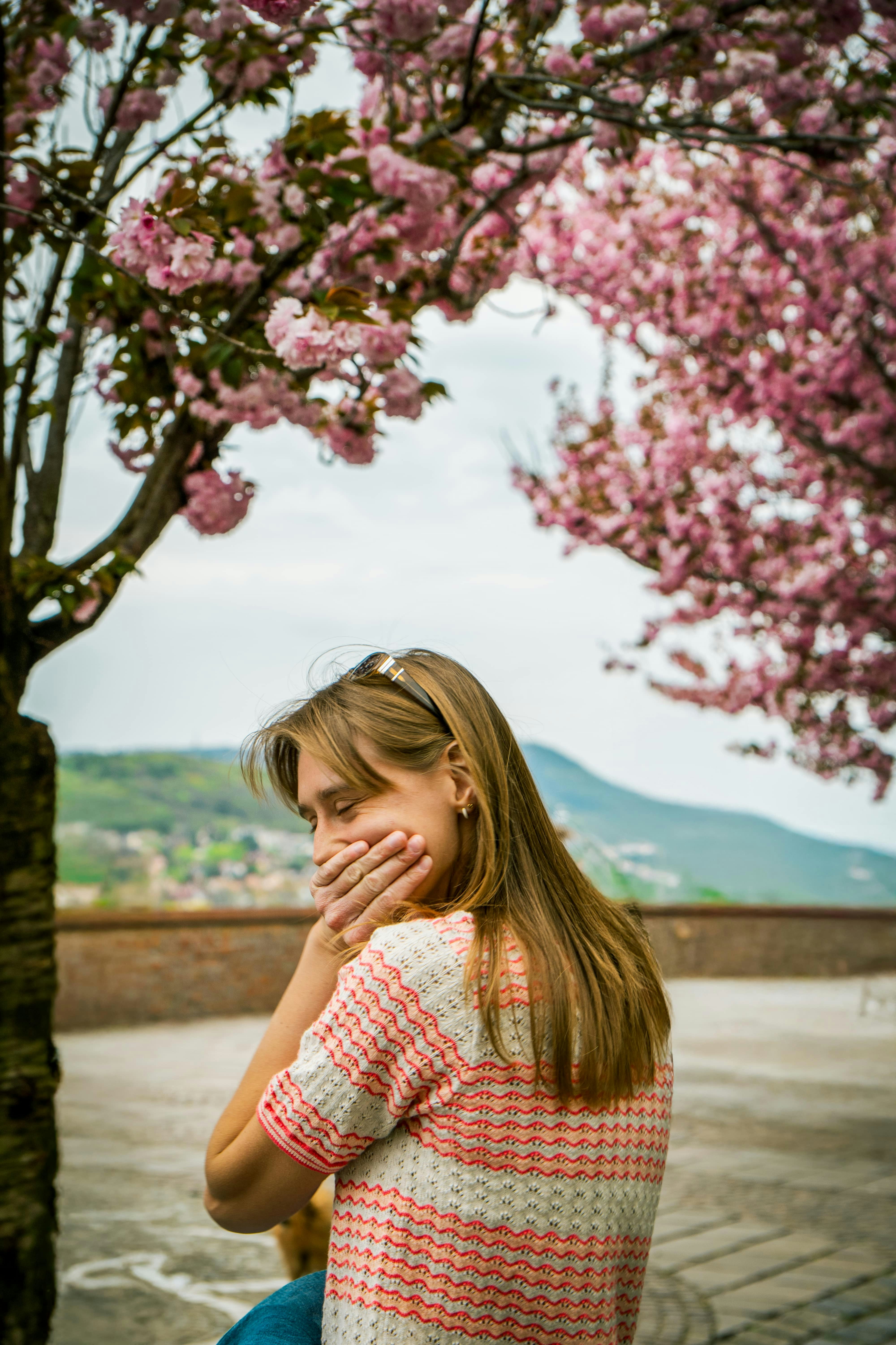 La mujer se cubre la boca bajo un árbol en flor.