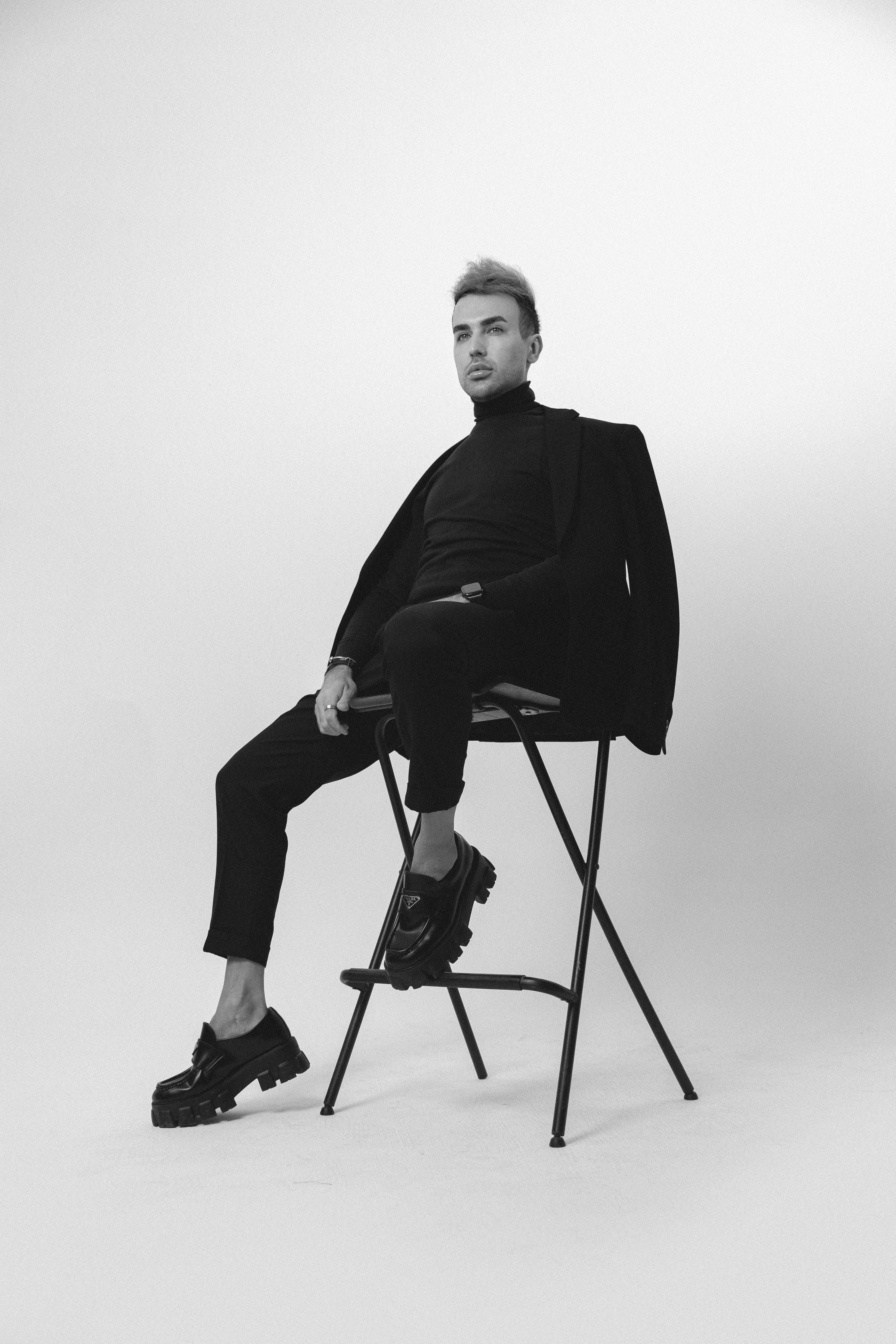 검은 양복을 입은 남자가 의자에서 포즈를 취하고 있습니다.