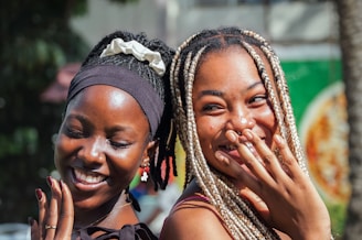 Two smiling women are close together outdoors.