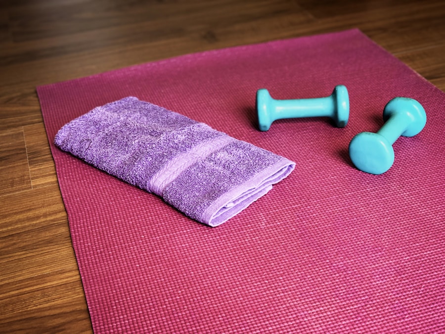Folded purple hand towel and two small dumbbells on a pink yoga mat