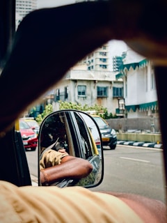 View from a rickshaw mirror shows city traffic.