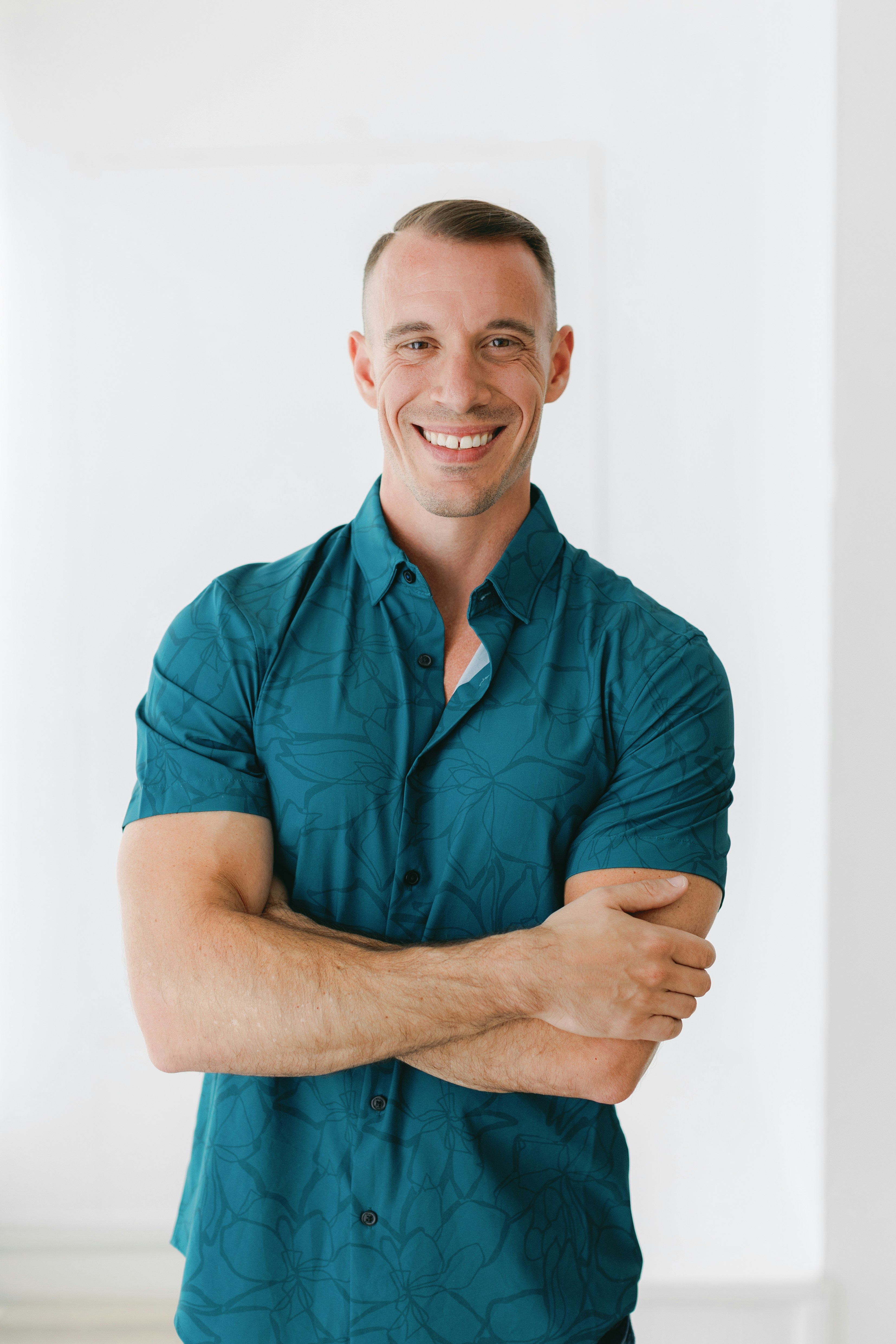 Un homme souriant se tient debout, les bras croisés.