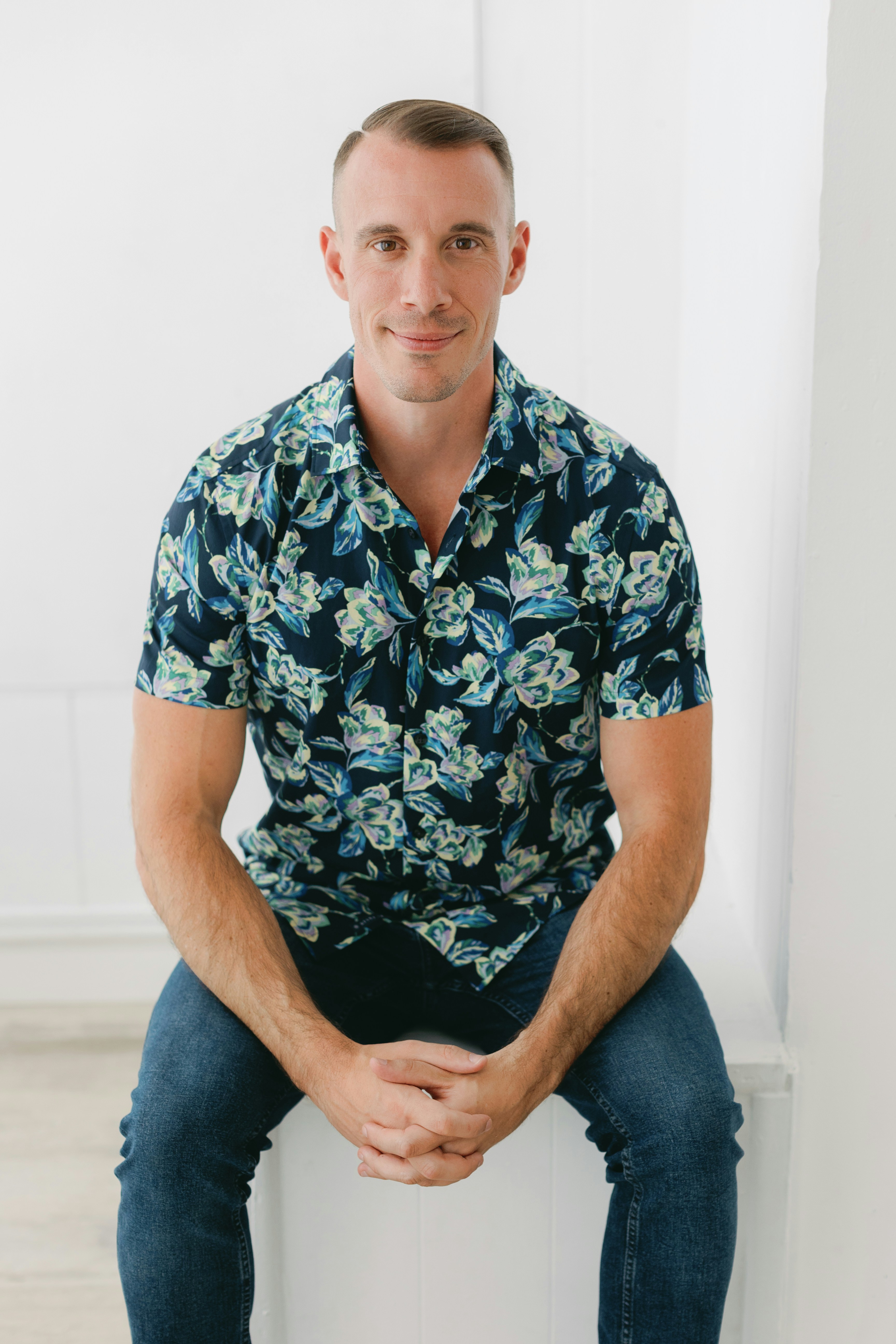 Un homme pose, vêtu d’une chemise à fleurs.