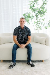 A smiling man sits on a white couch.
