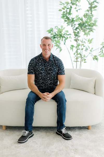 A smiling man sits on a white couch.