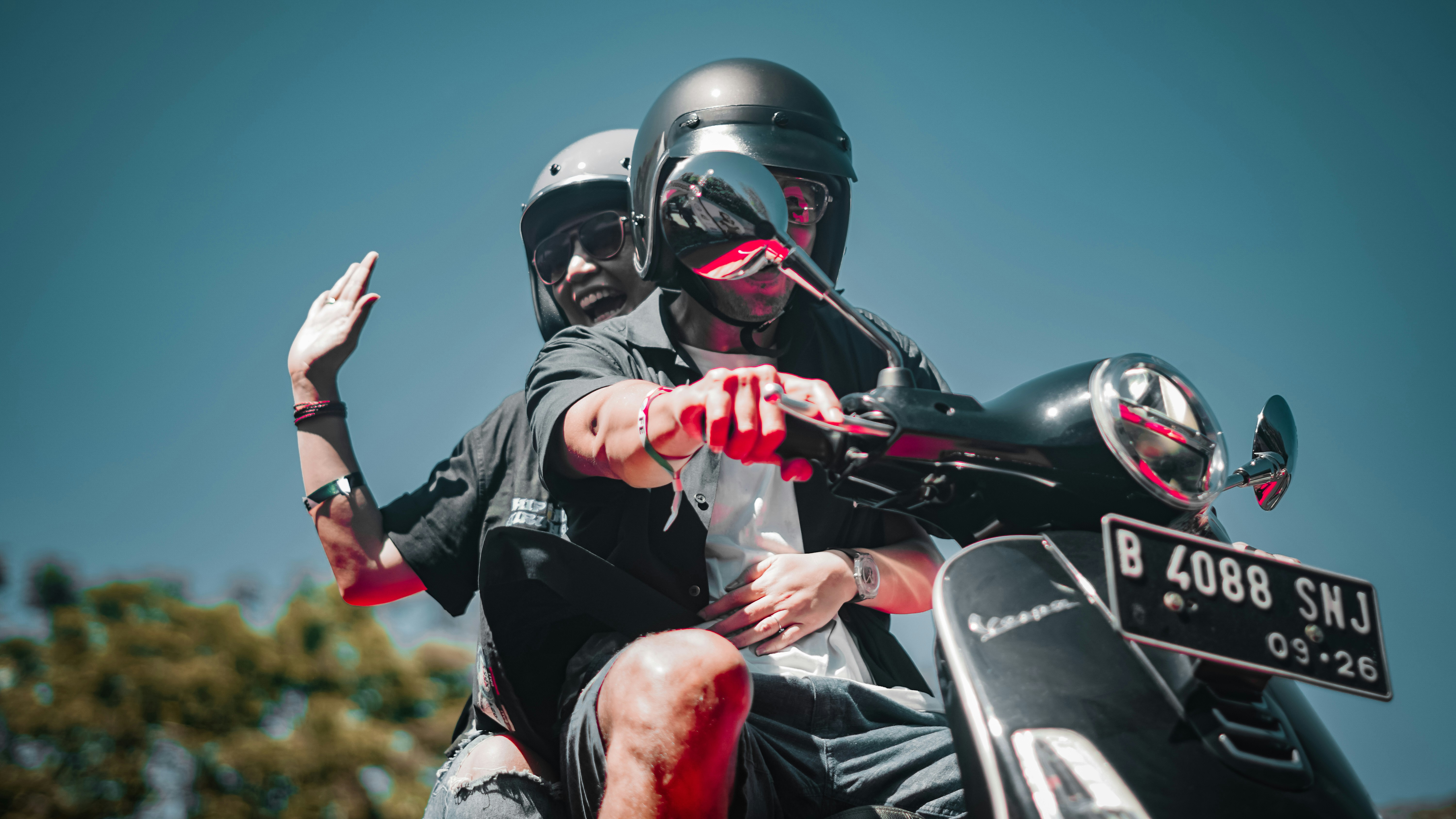 Two people ride a scooter on a sunny day.