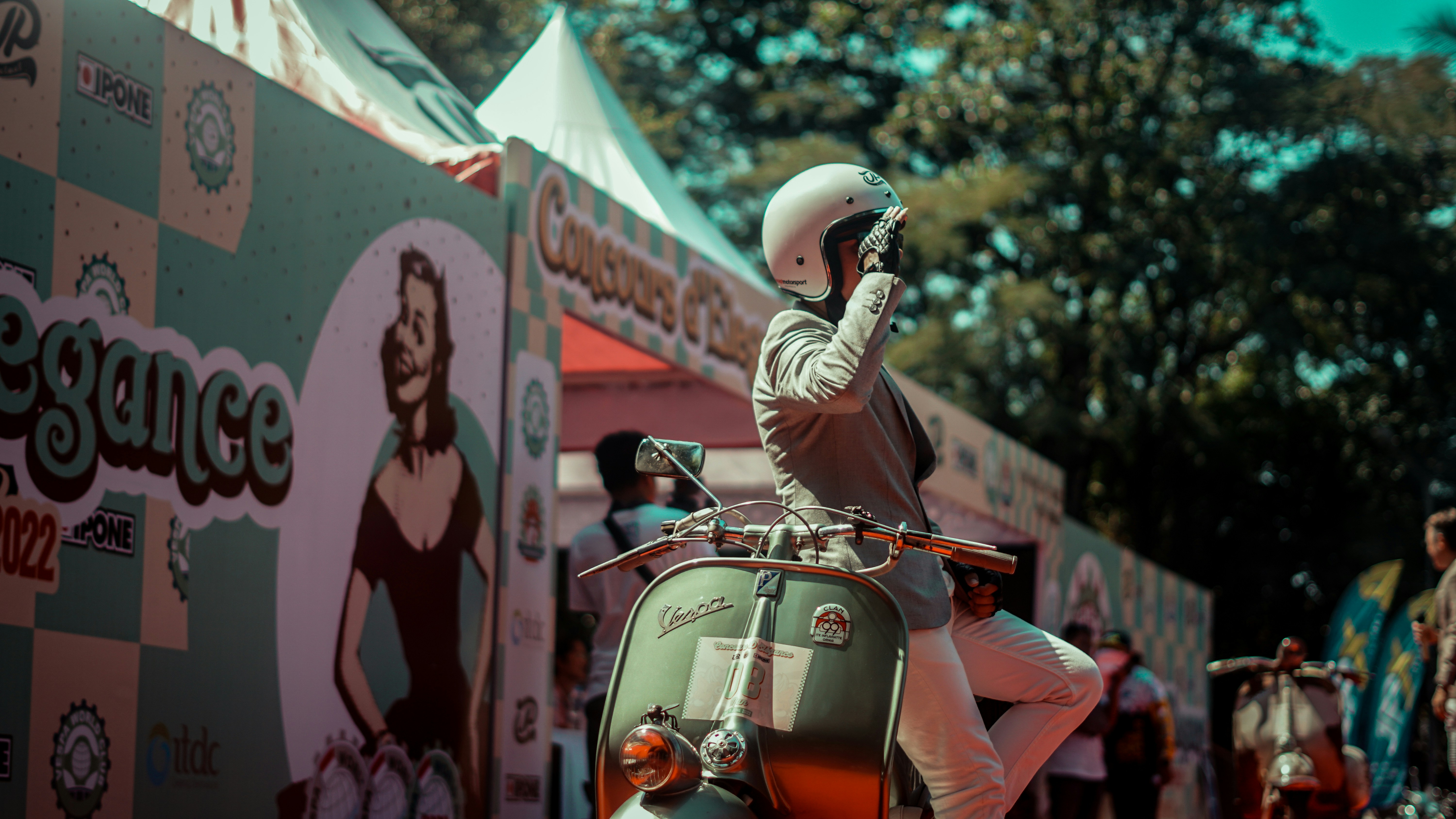 A person in a helmet poses on a vespa.