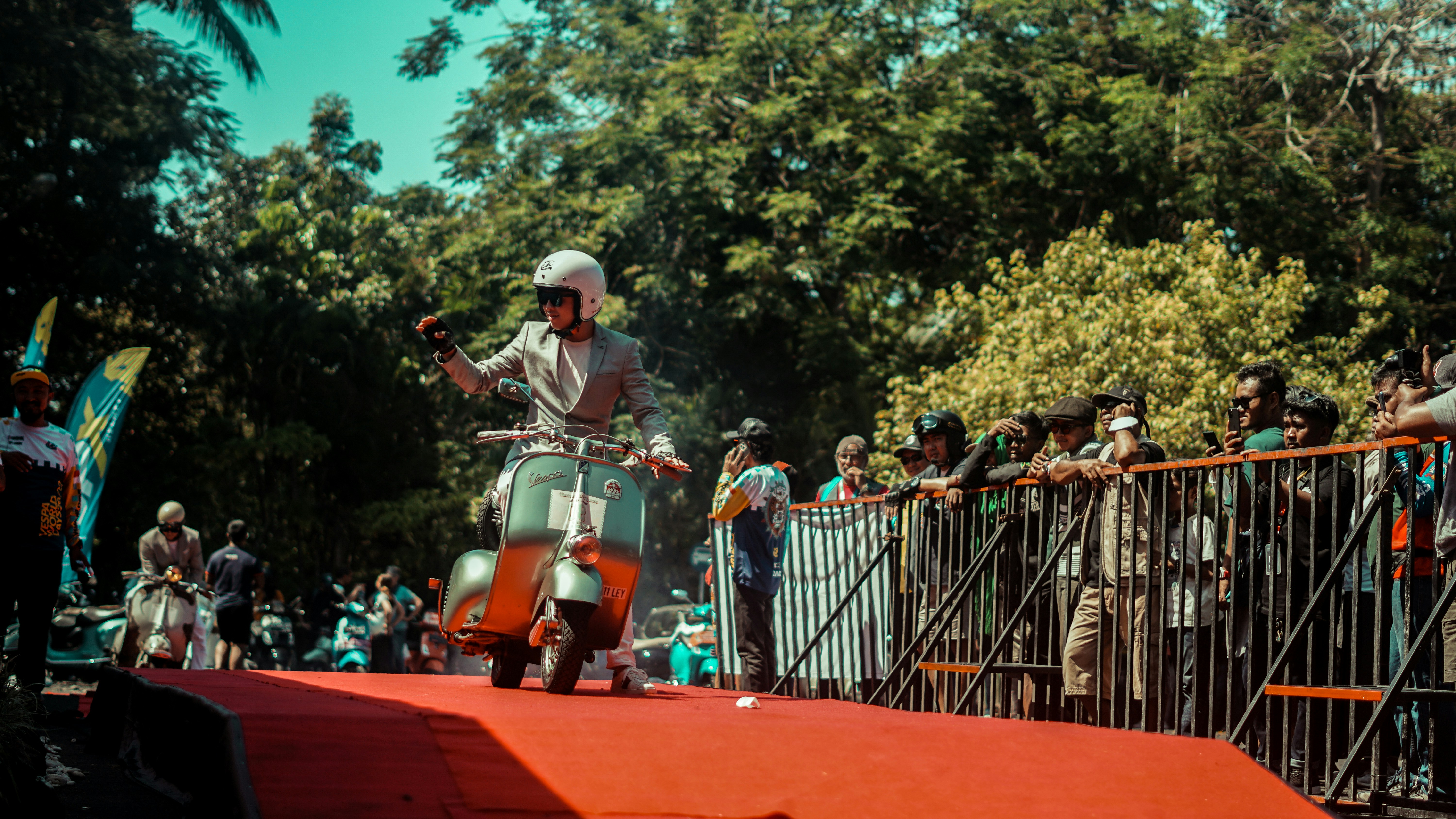 A man rides a scooter on a red carpet.