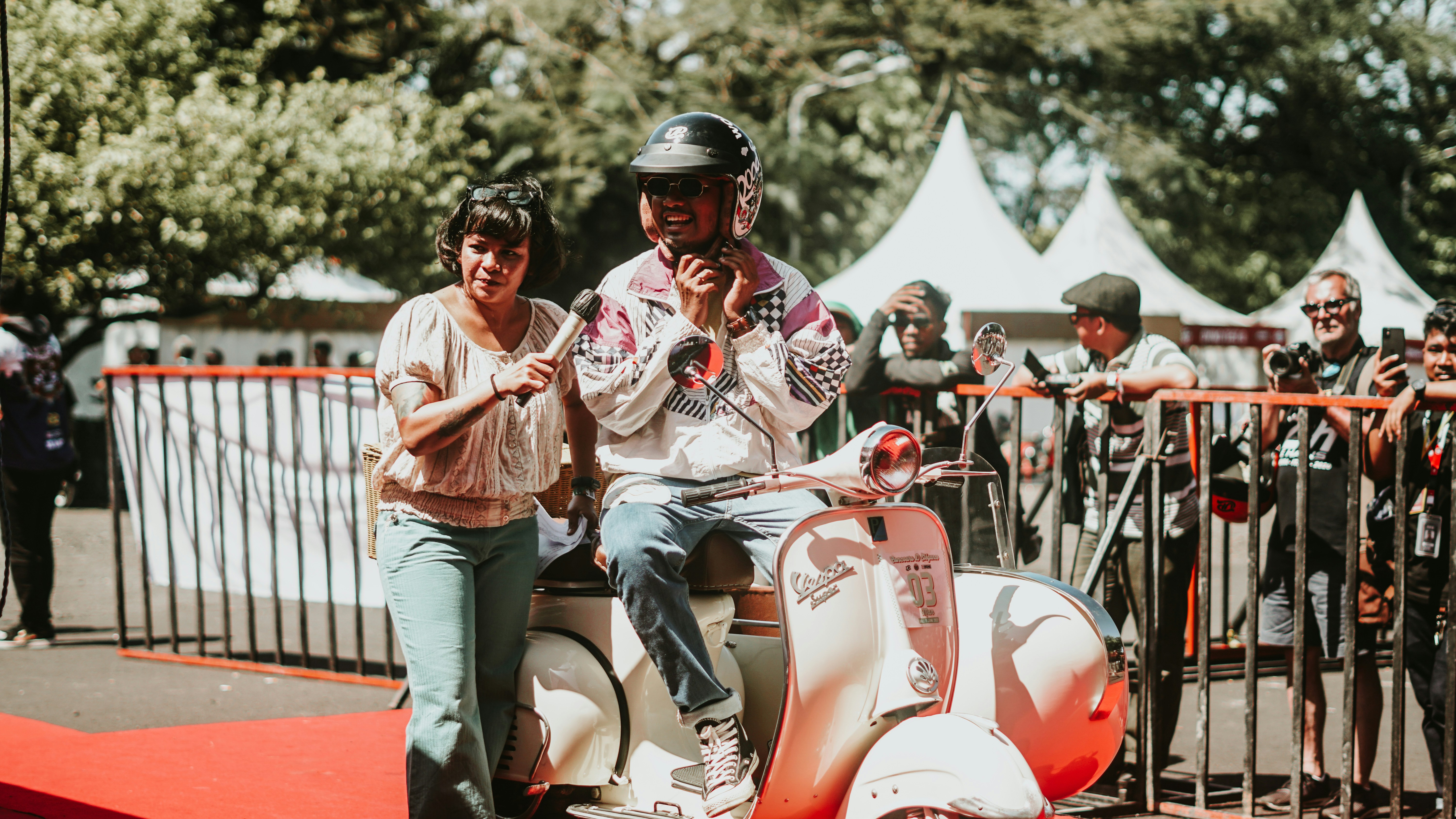 A person sits on a scooter with a companion.