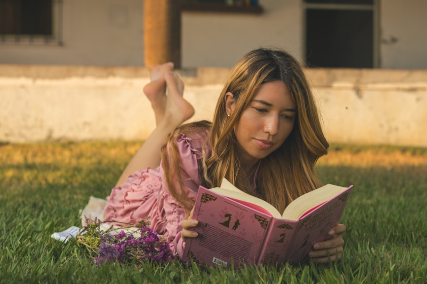 Woman enjoys a book while lounging in the grass.