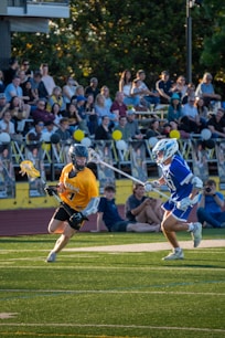 Lacrosse players compete on the field with a crowd.