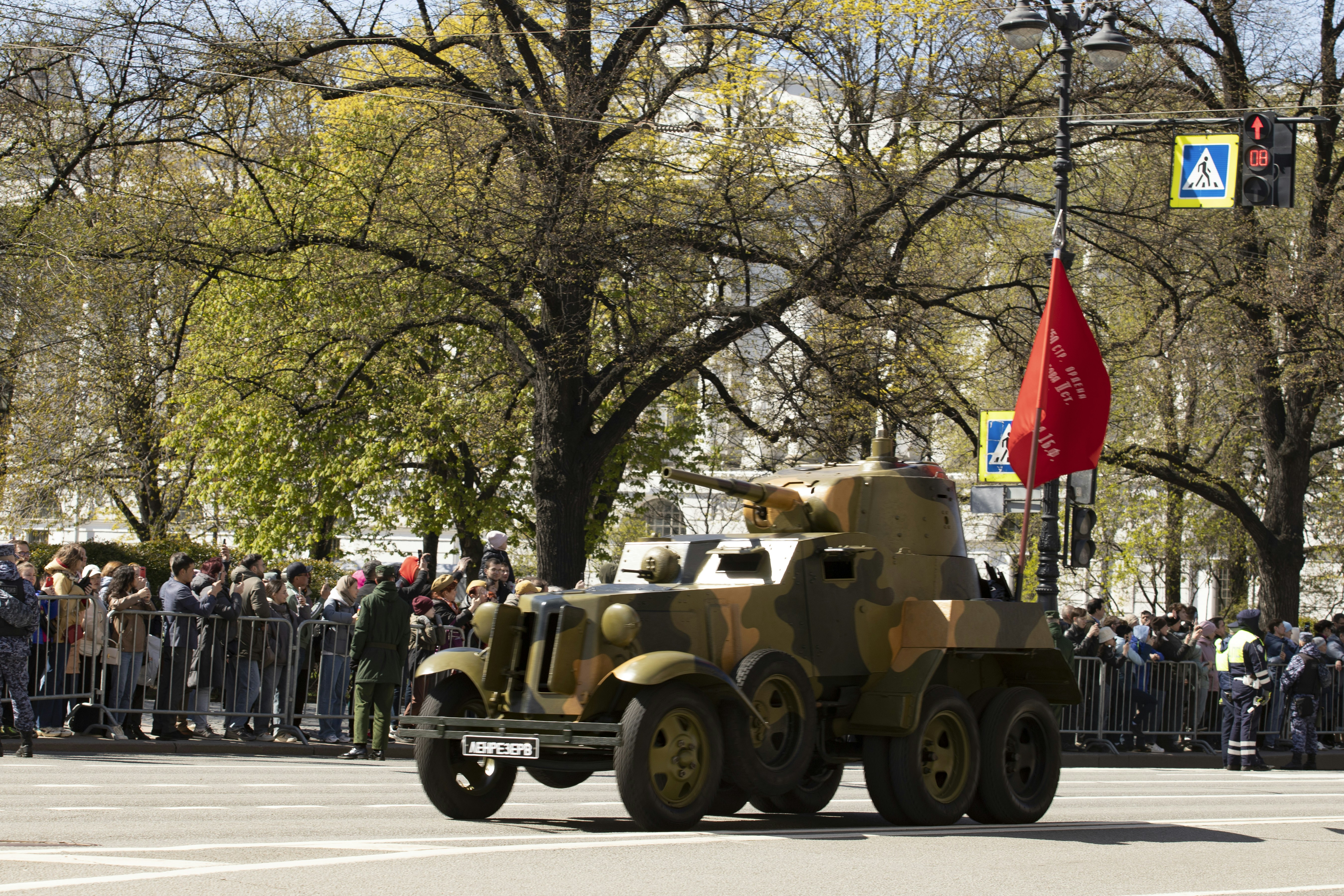 A camouflaged armored car drives through a crowd. (Photo by Maria Baranova on Unsplash)