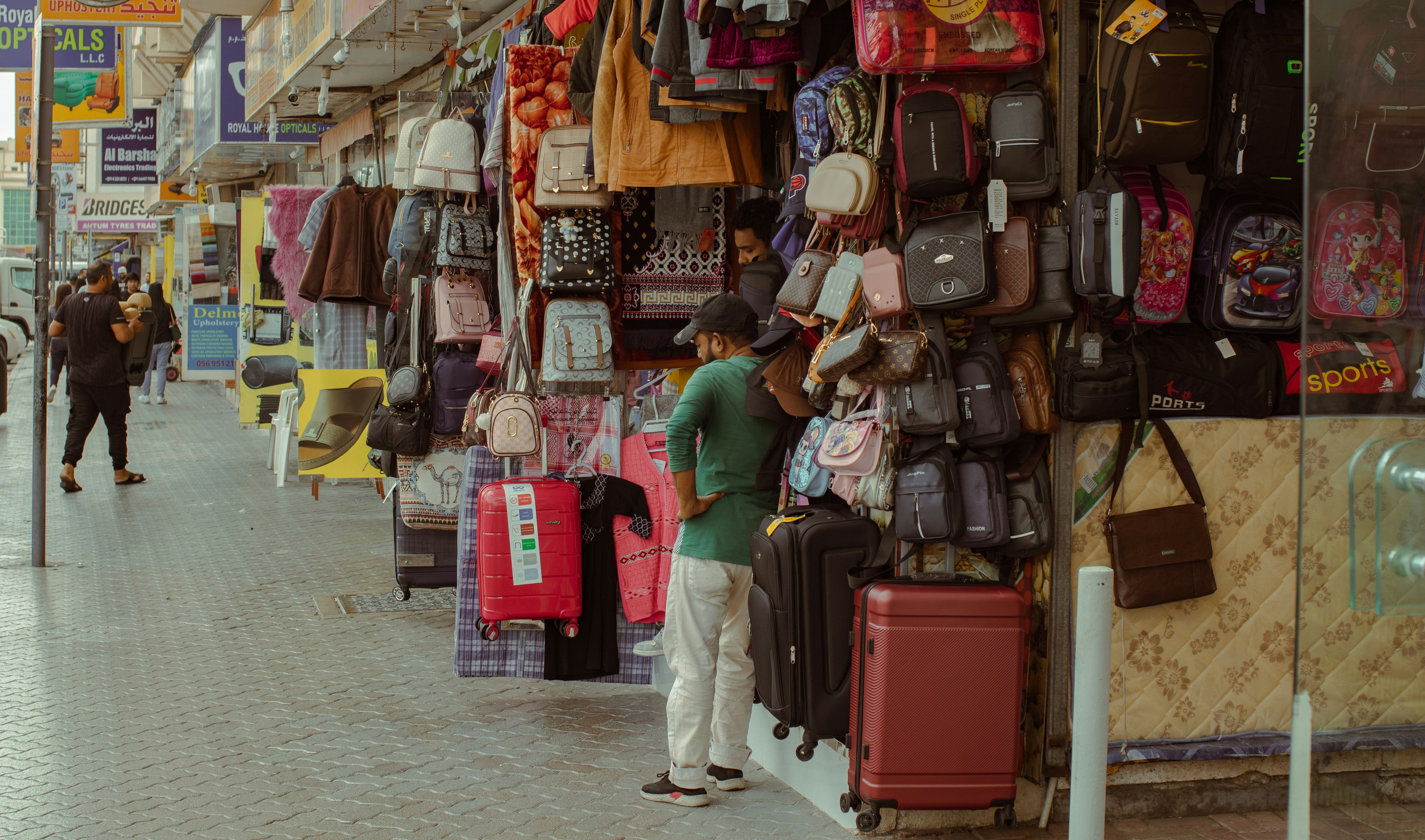 A man browses bags and luggage at a market stall.