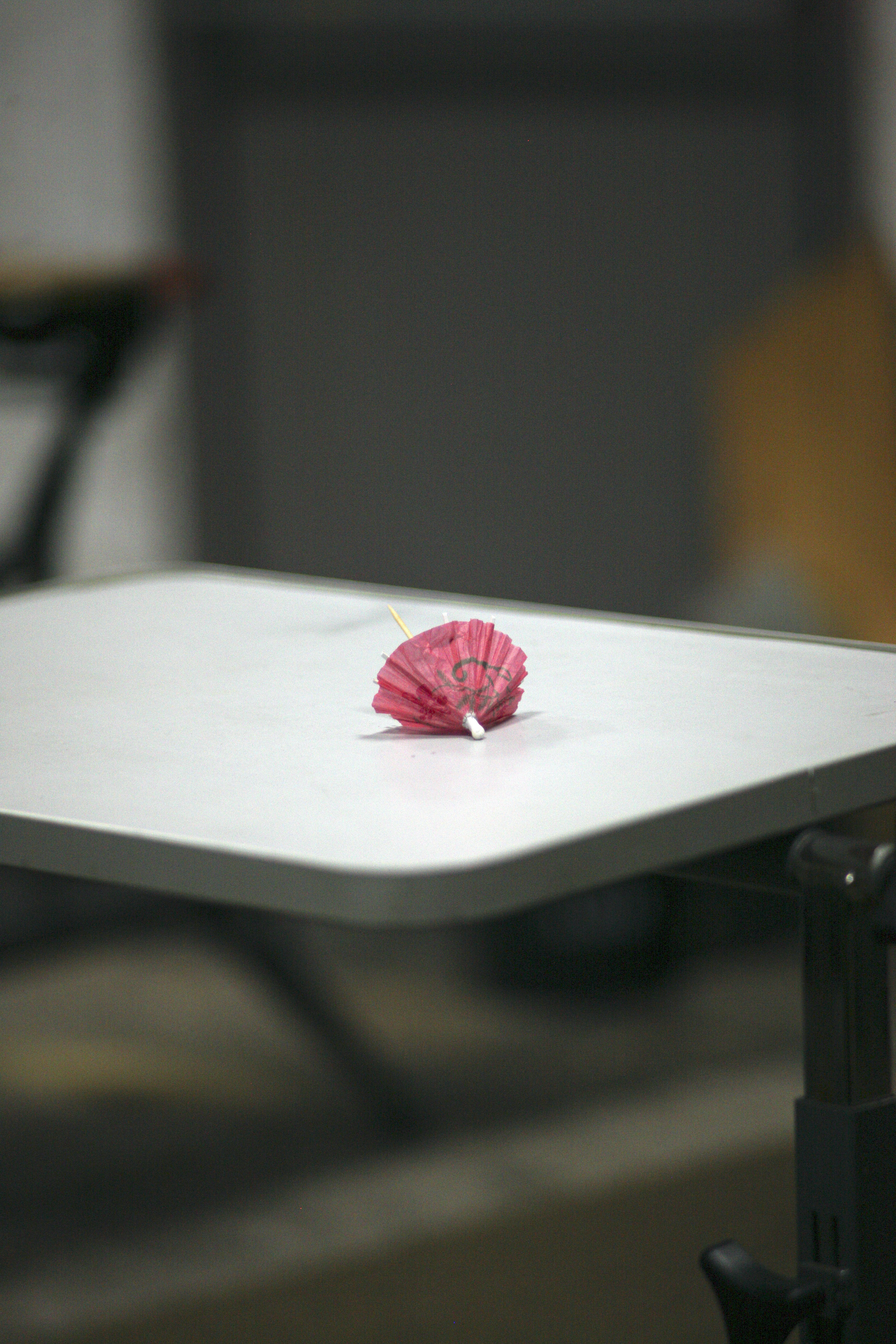 Une fleur rose en origami est posée sur une table blanche.