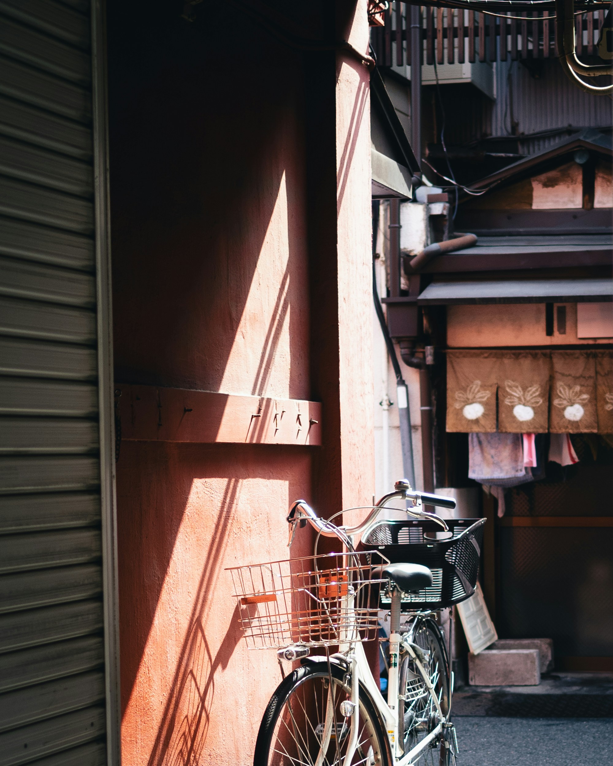 A bicycle rests next to a sunlit, red wall.