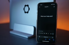 Phone displays chatgpt, next to laptop.