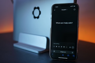 Phone displays chatgpt, next to laptop.