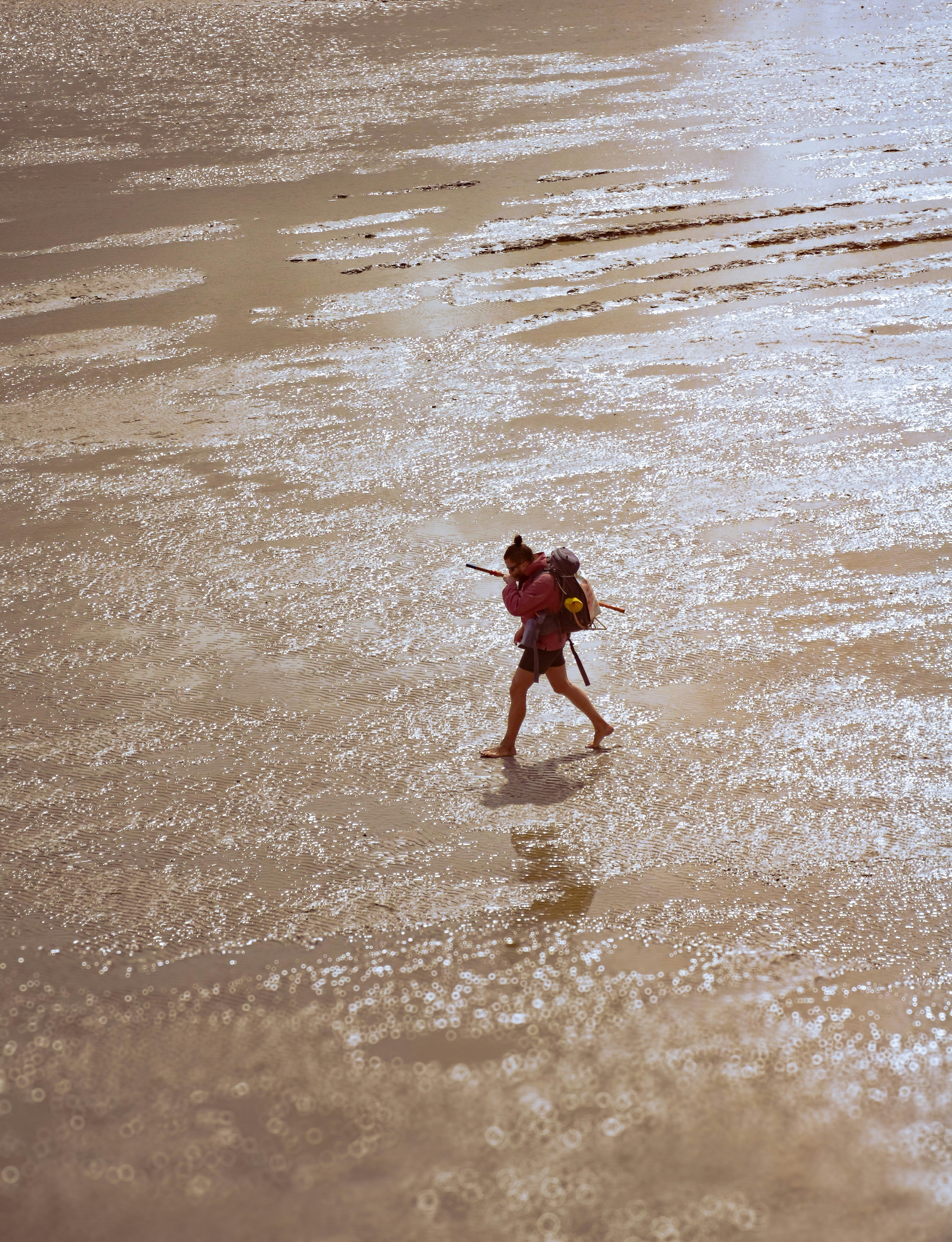 A person walks across a wet, sandy beach.