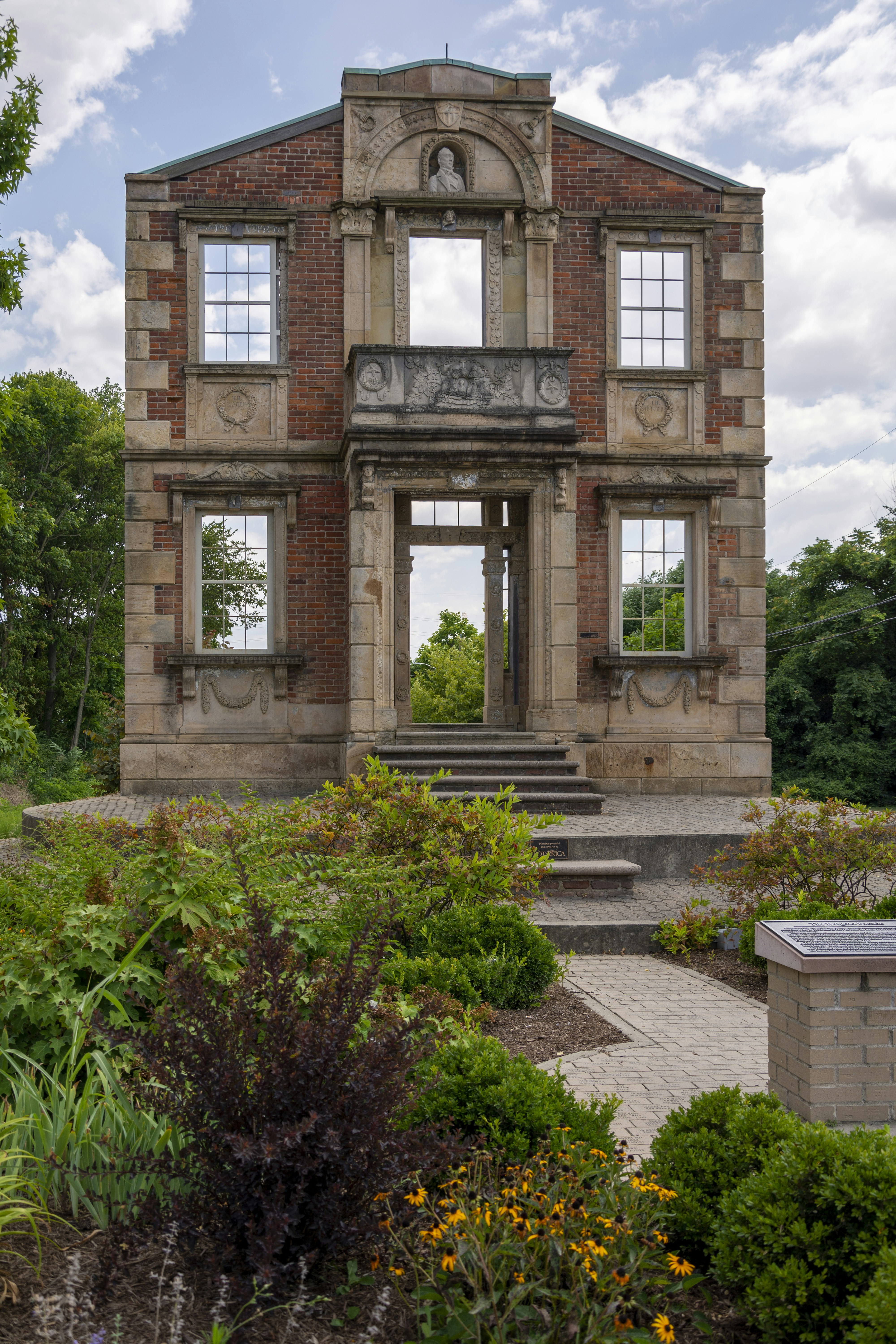 A stone facade stands in front of lush greenery.
