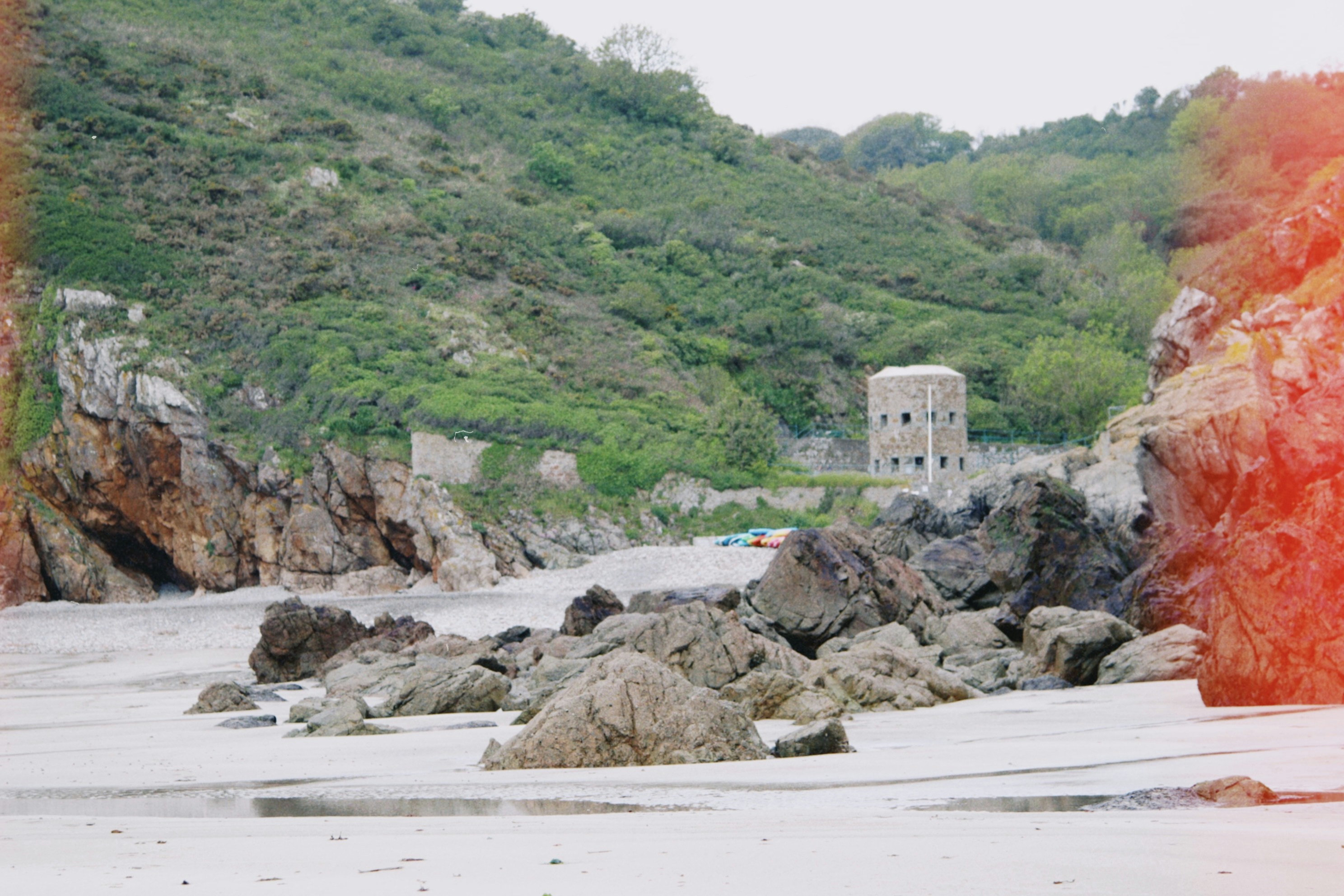 Rocky beach with hills and a tower.