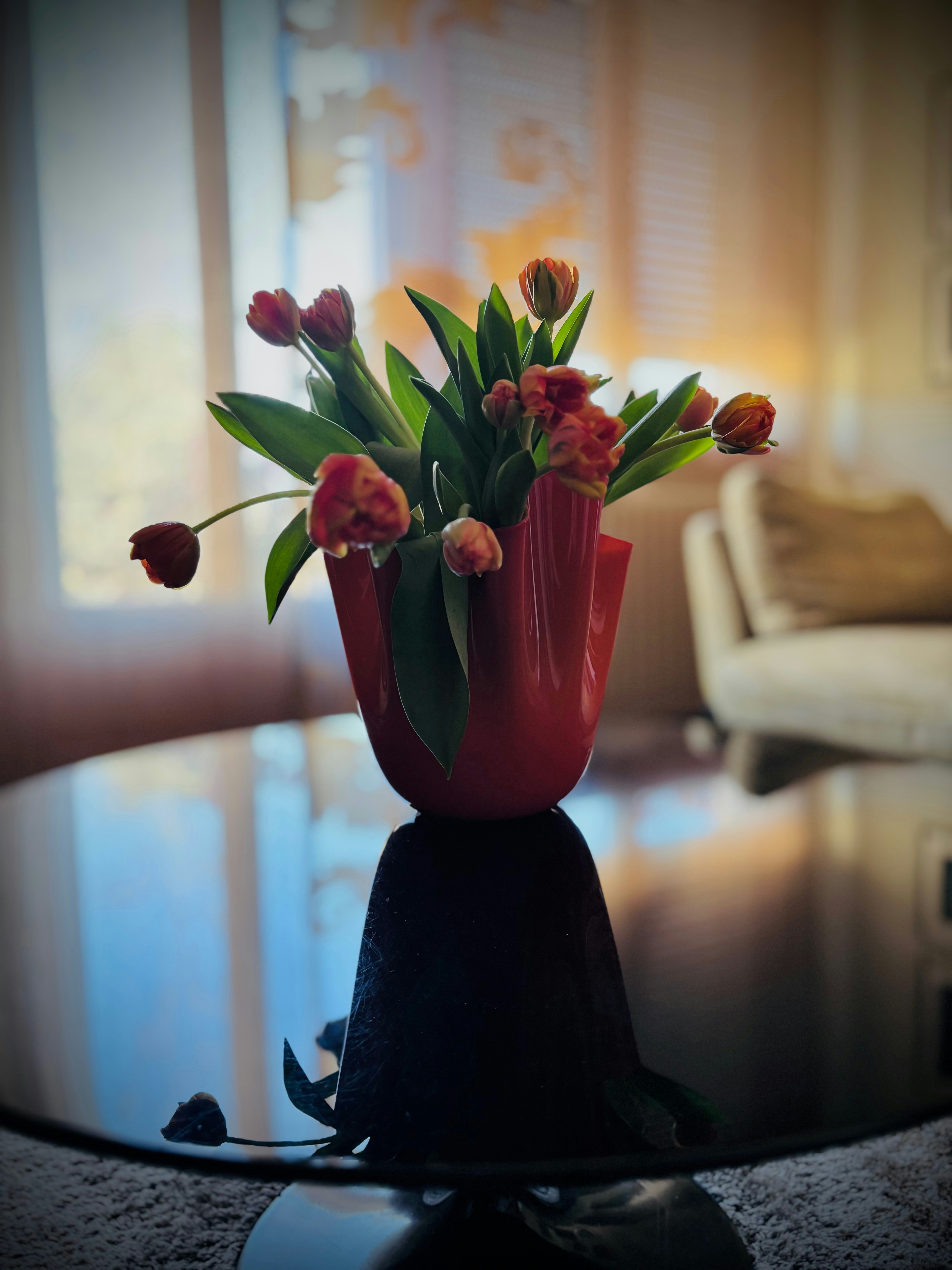 Tulips in a vase reflect on a dark table.