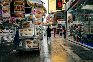 A street food cart sits on a wet city street.