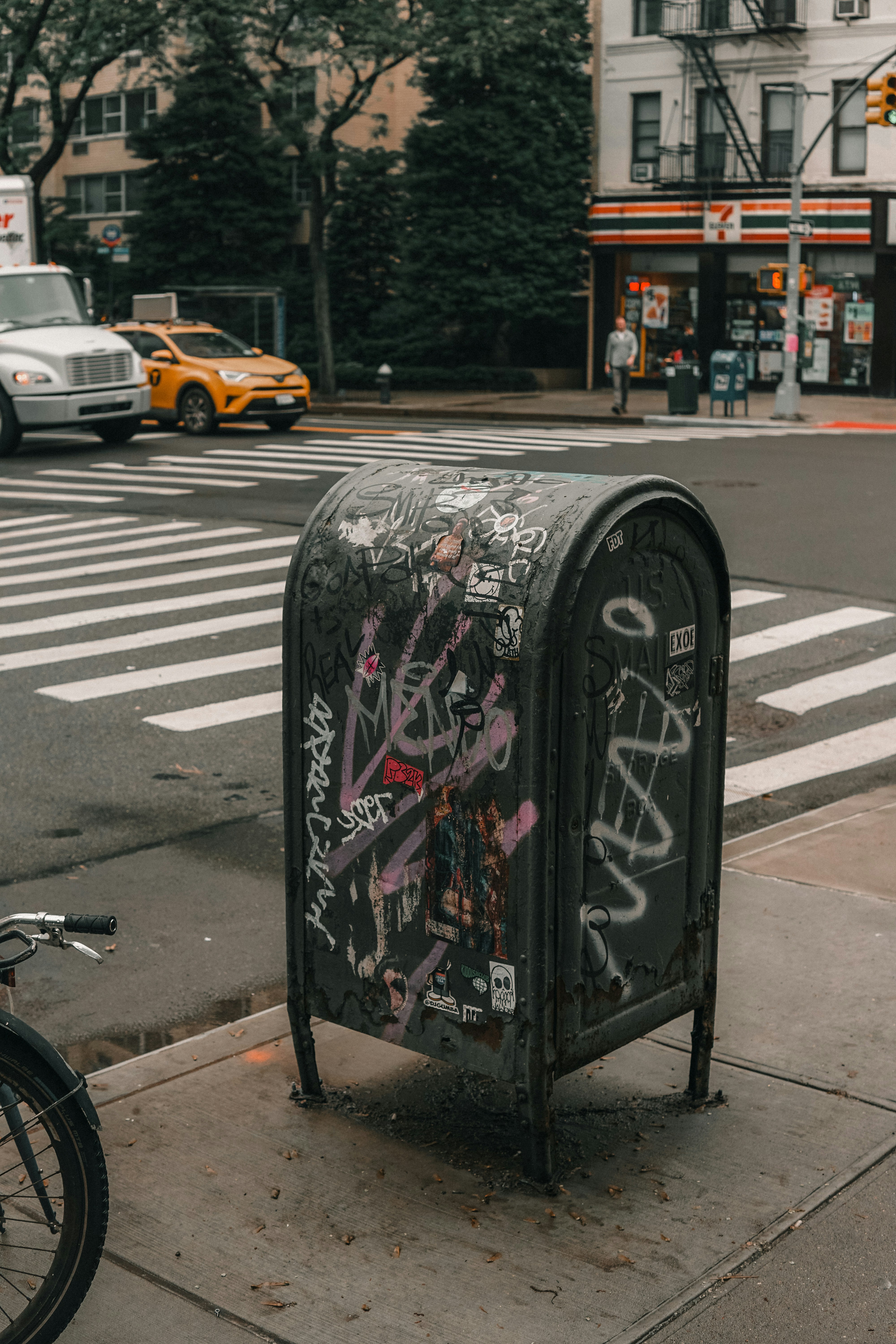 Graffiti-covered mailbox on a city street corner.