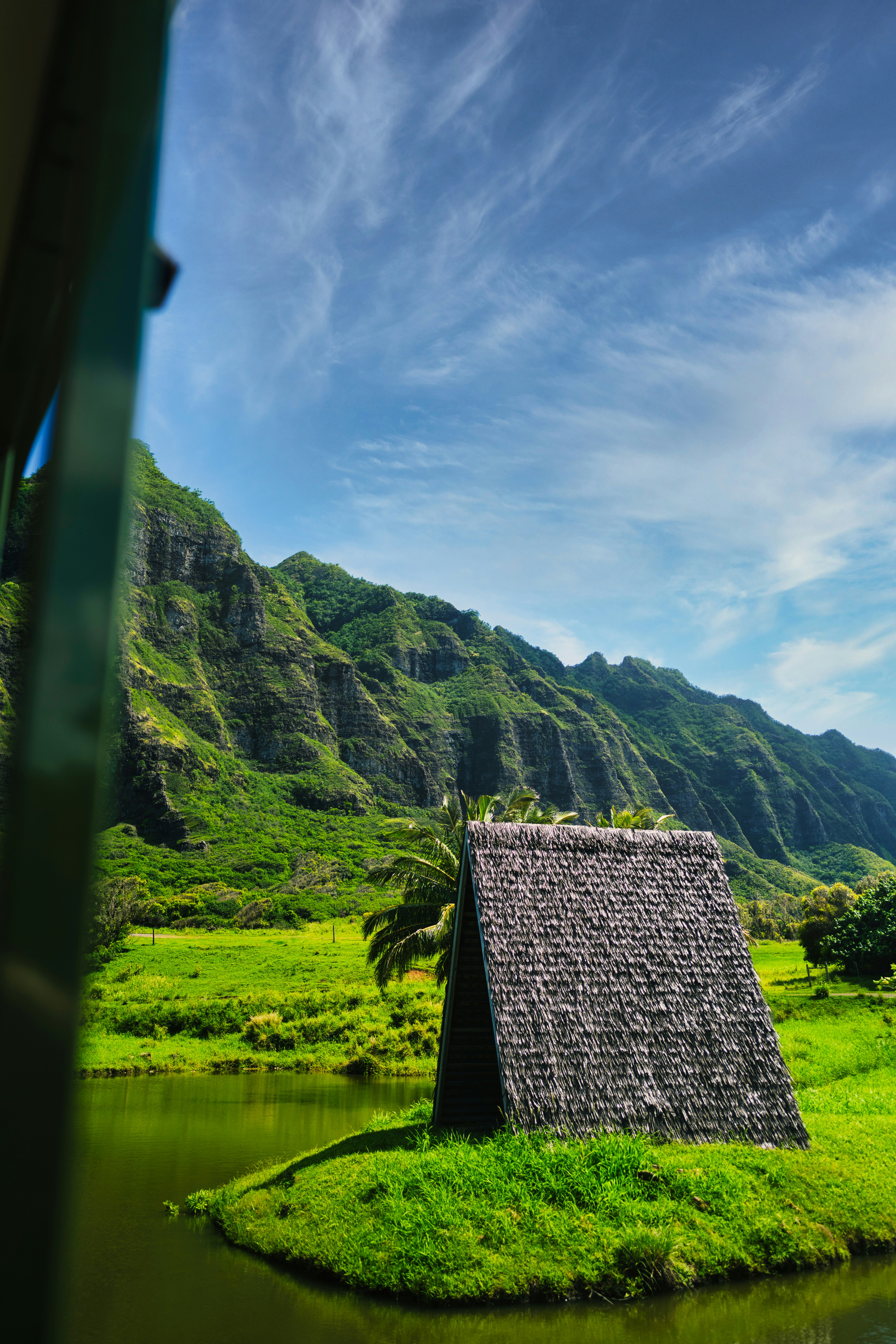 Green mountains overlook a grassy area with a hut.