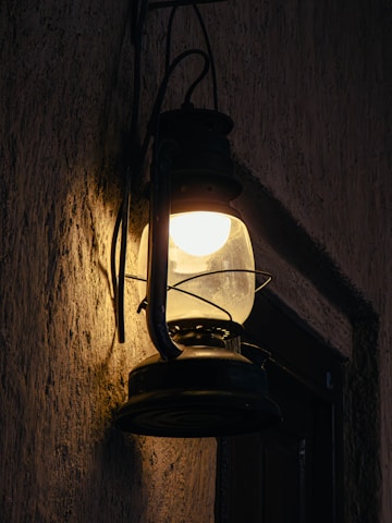 A vintage lantern glows against a dark wall.