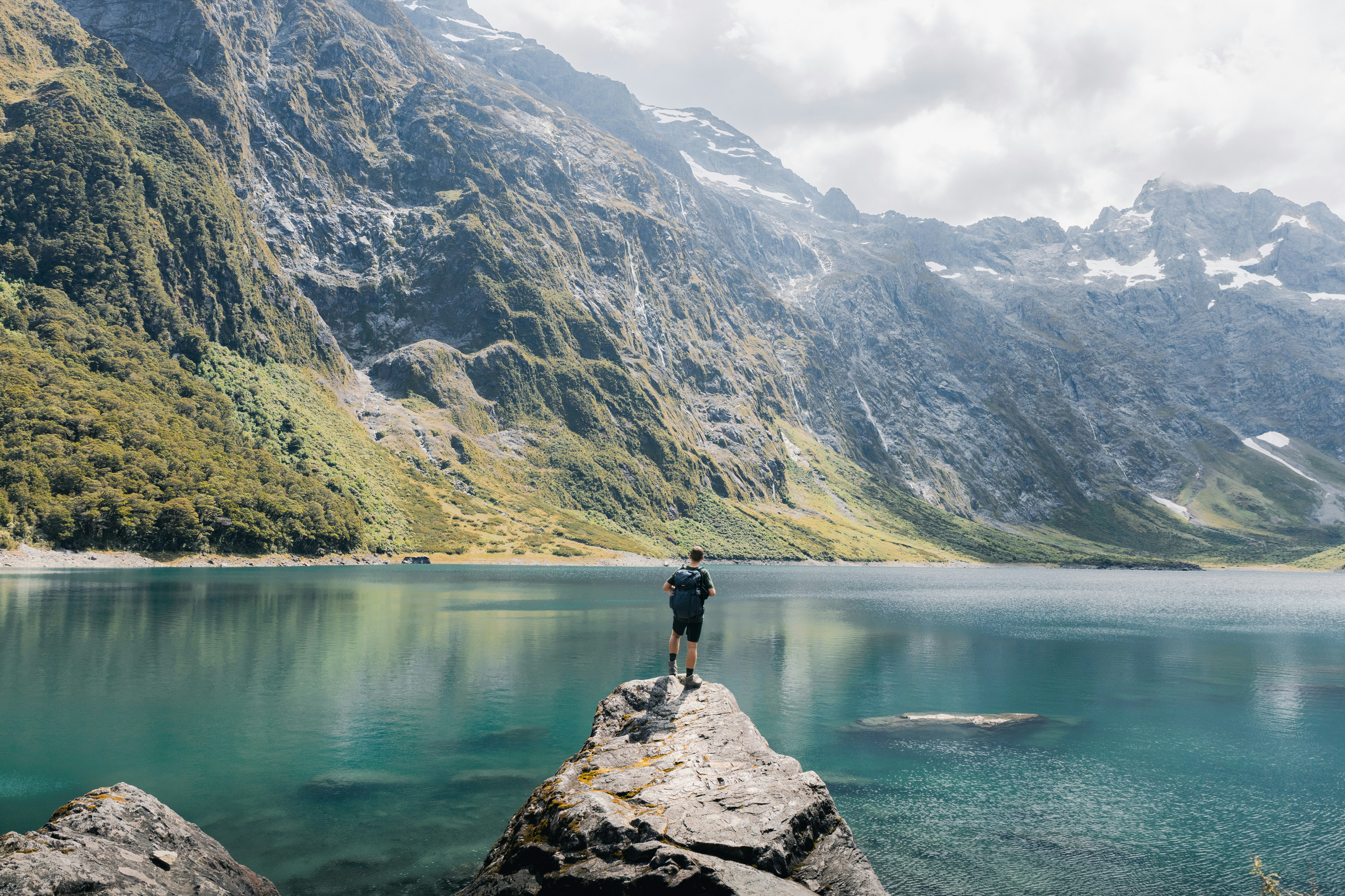 El hombre está de pie sobre una roca con vistas a un hermoso lago.