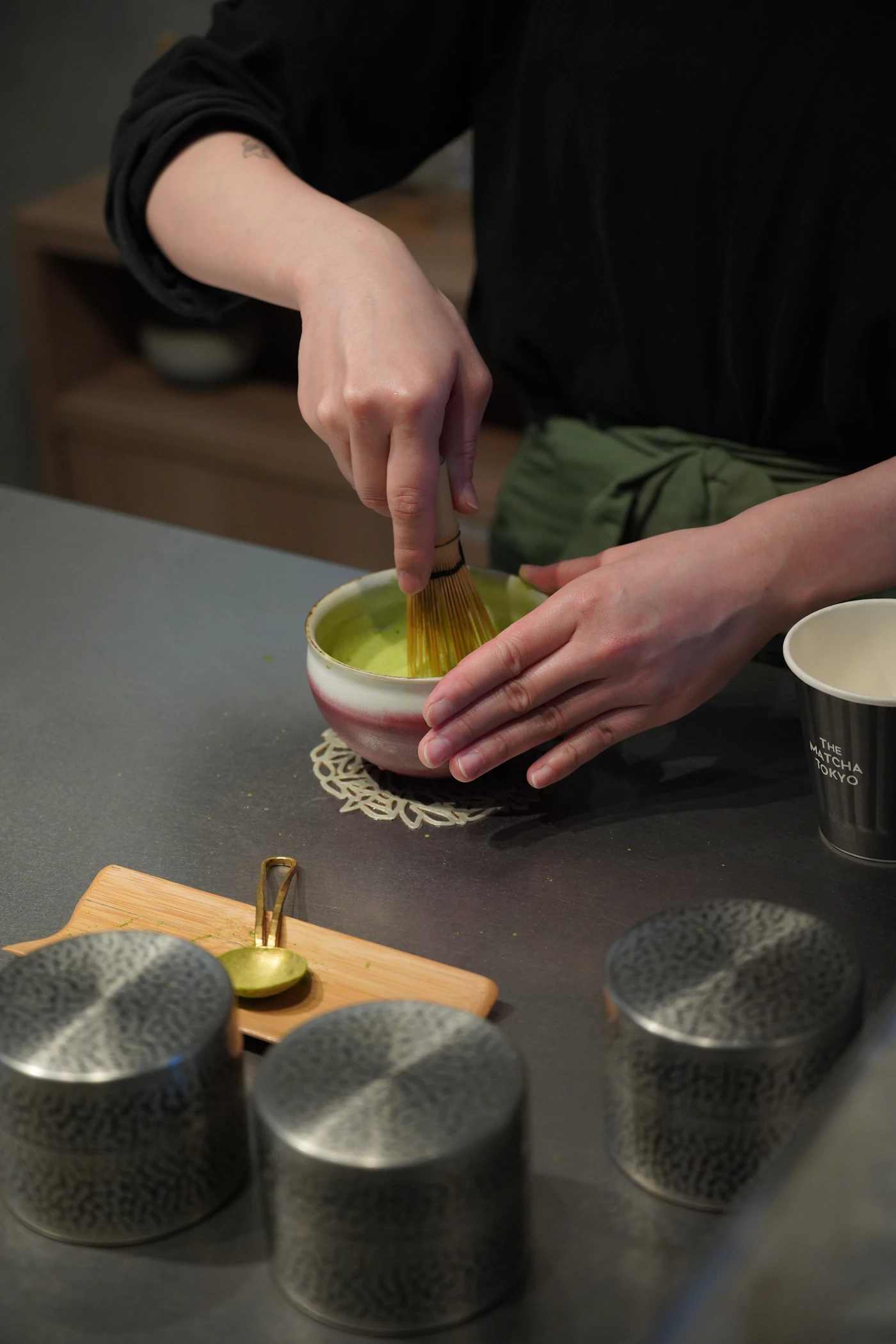 Hands whisking bright green matcha in a ceramic bowl