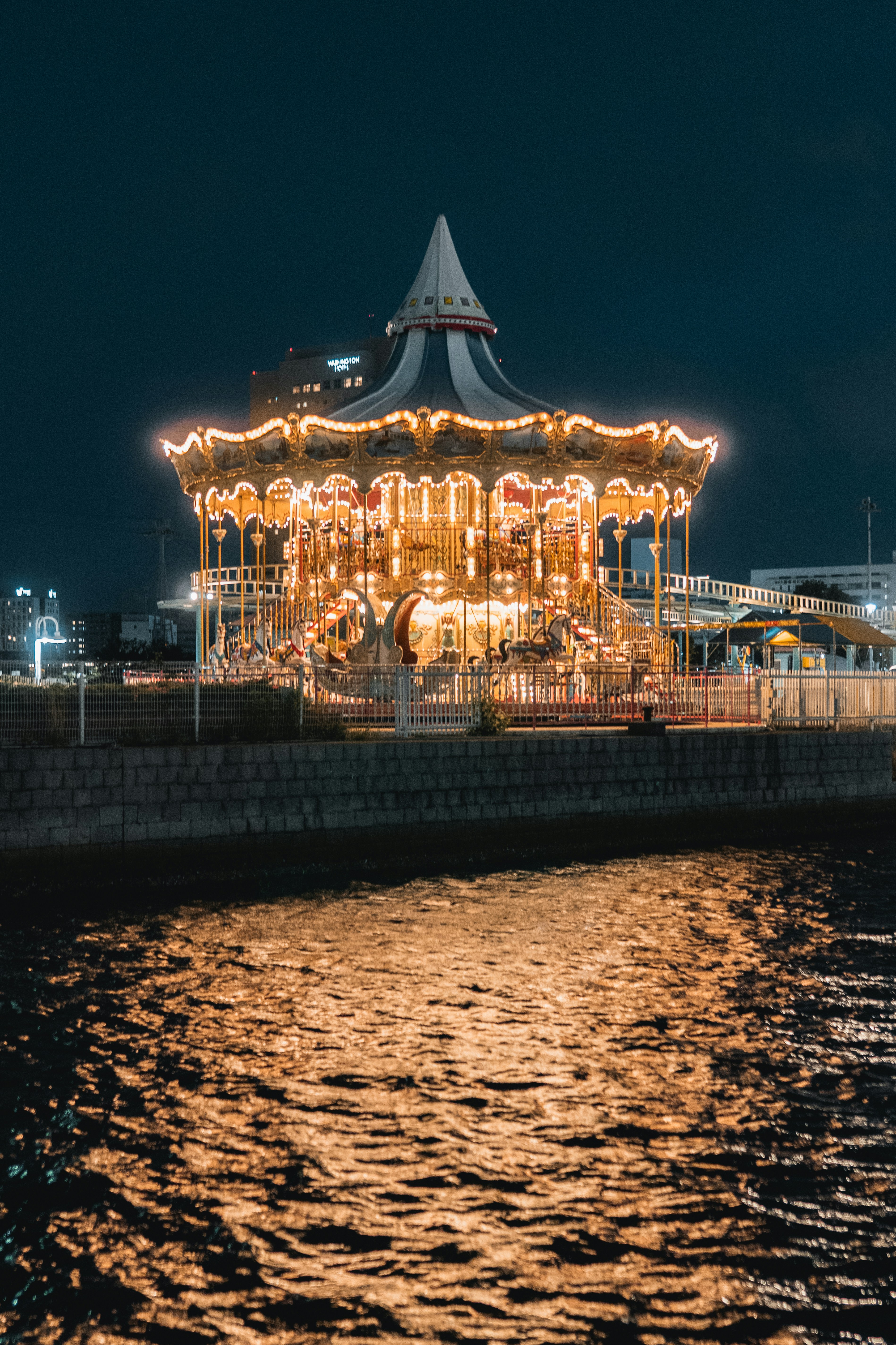 A lit-up carousel reflects in the water at night.