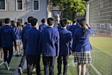 Students in uniform are walking near a sports field.