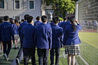 Students in uniform are walking near a sports field