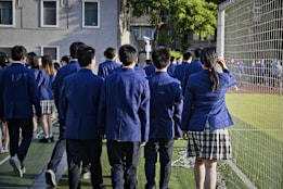 Students in uniform are walking near a sports field.