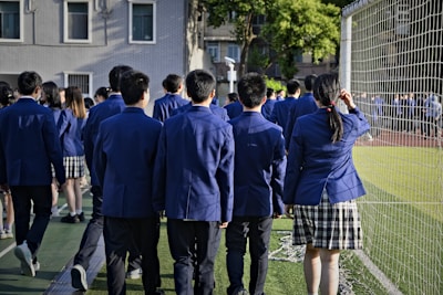 Students in uniform are walking near a sports field.