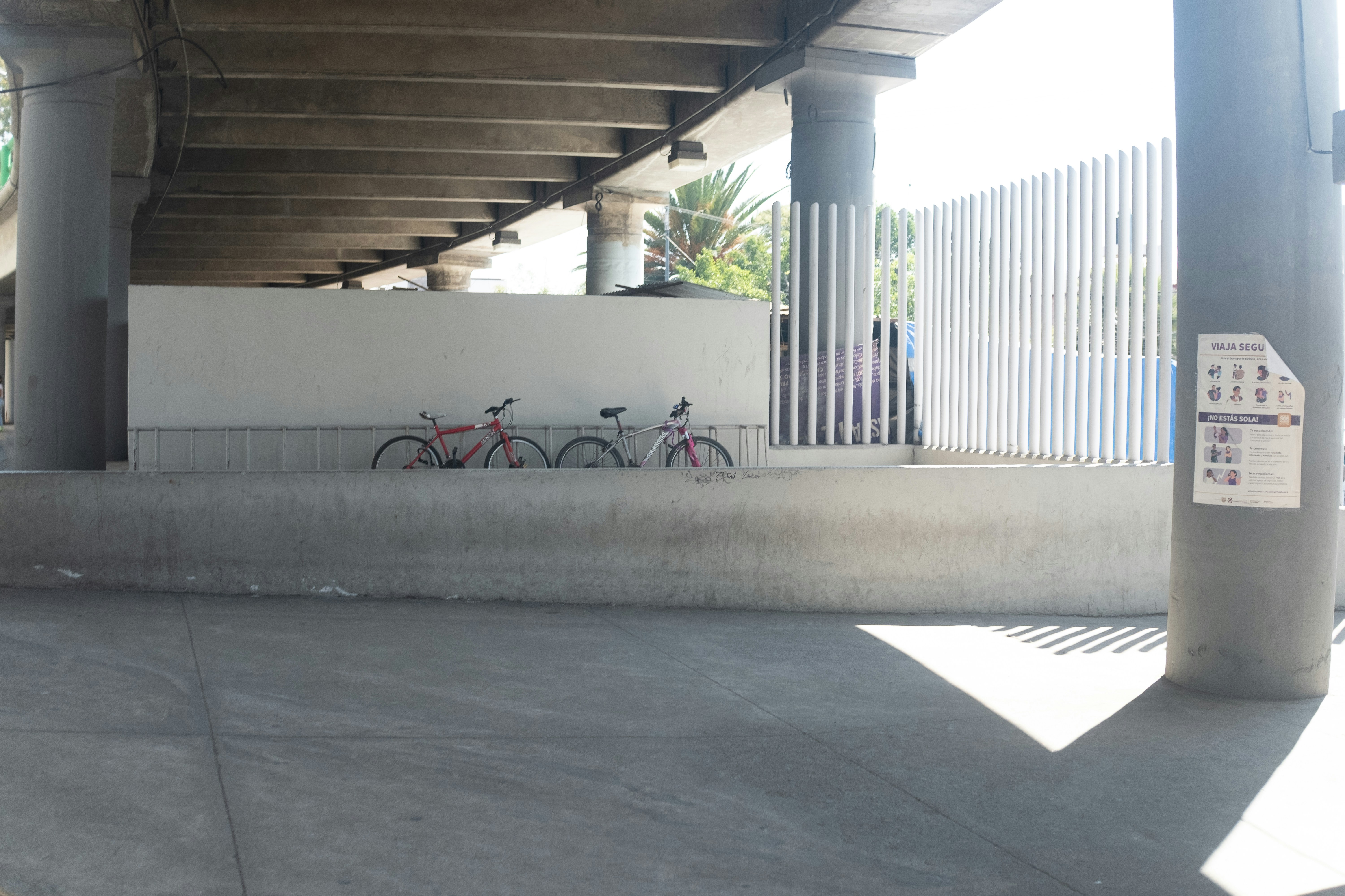 Two bicycles parked under a concrete overpass.