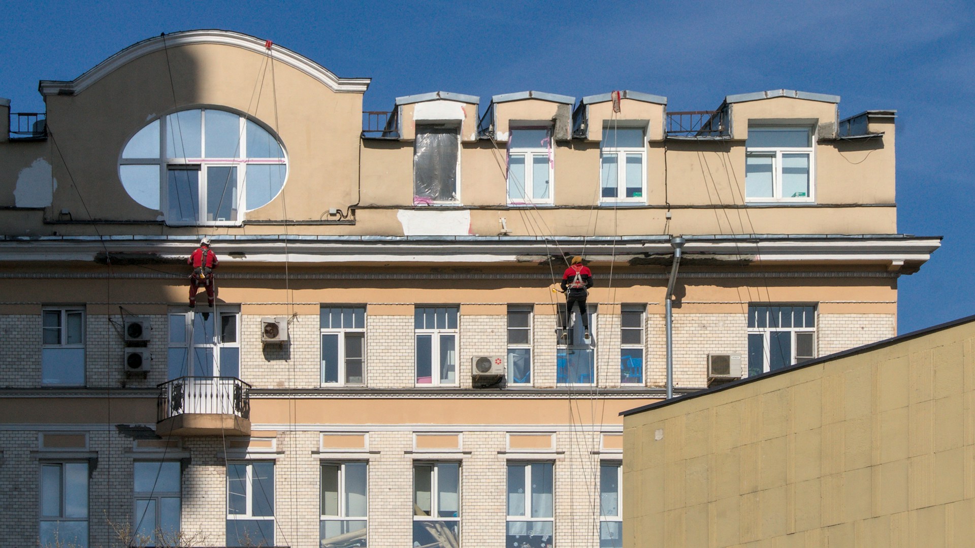 Workers paint the side of a large building.
