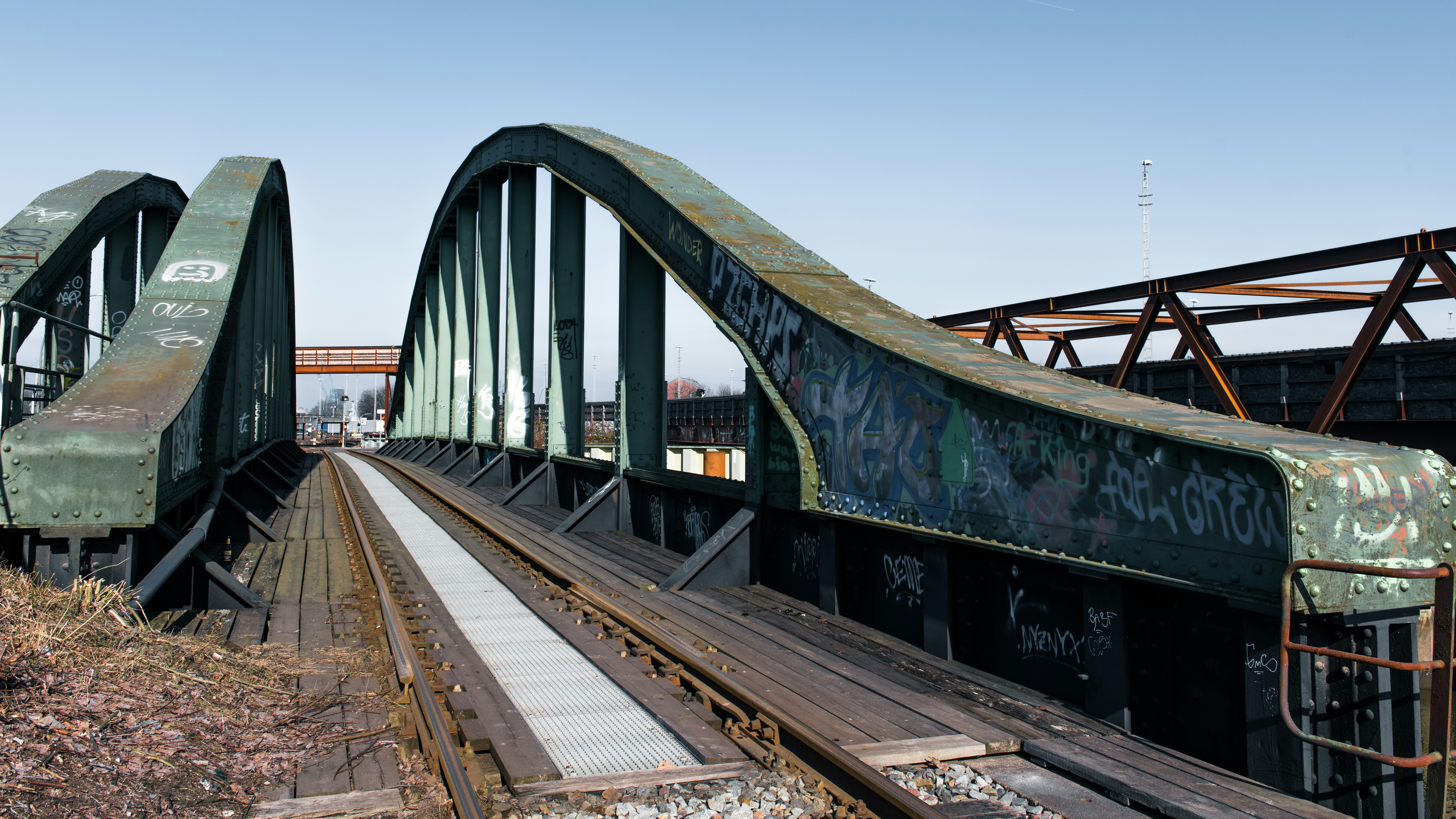 A railway bridge spans tracks under a blue sky.