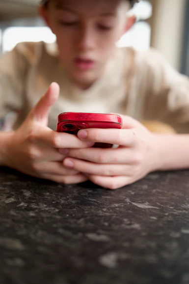 A boy focuses on his red cellphone.