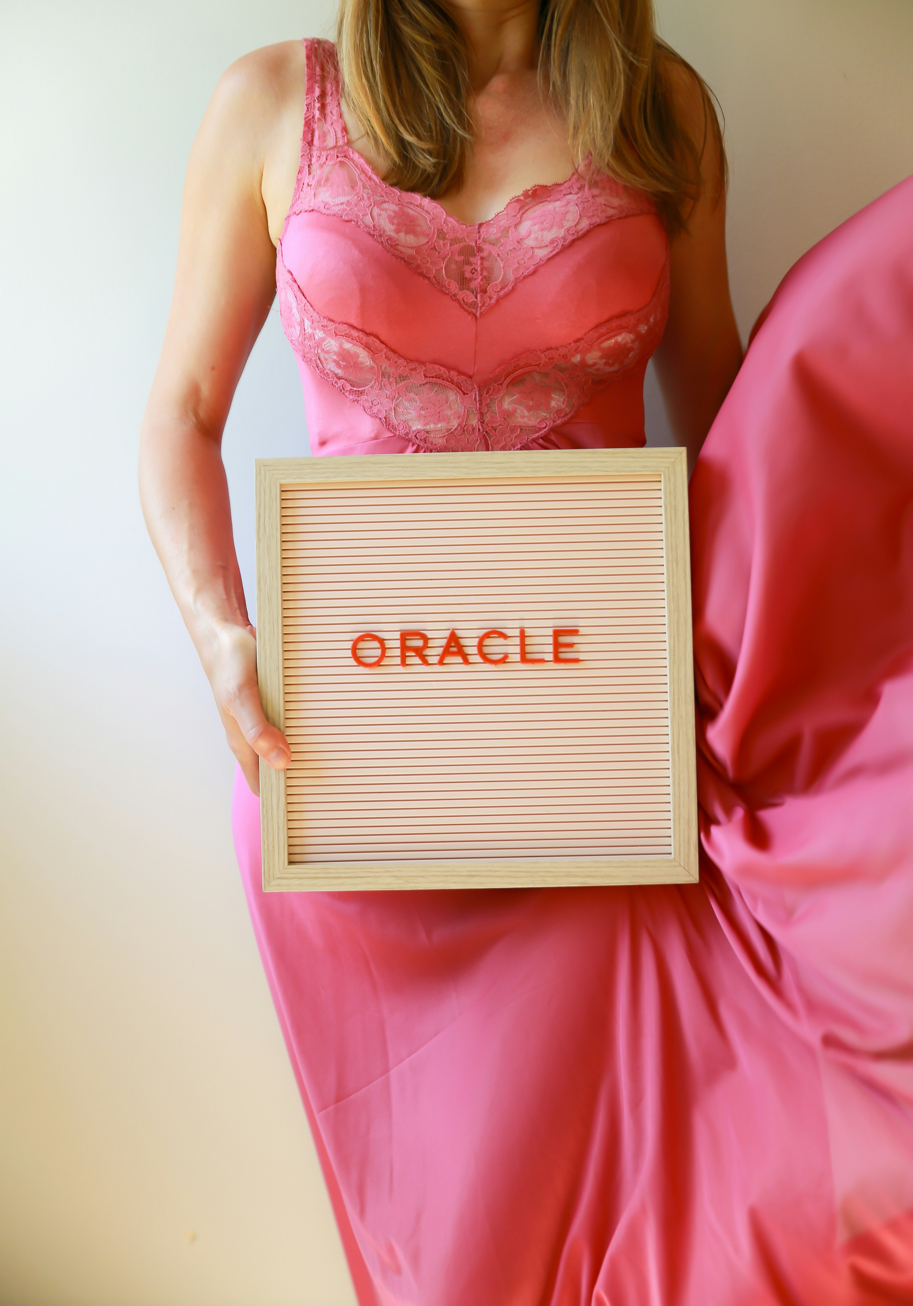 Woman in pink dress holds "oracle" sign.