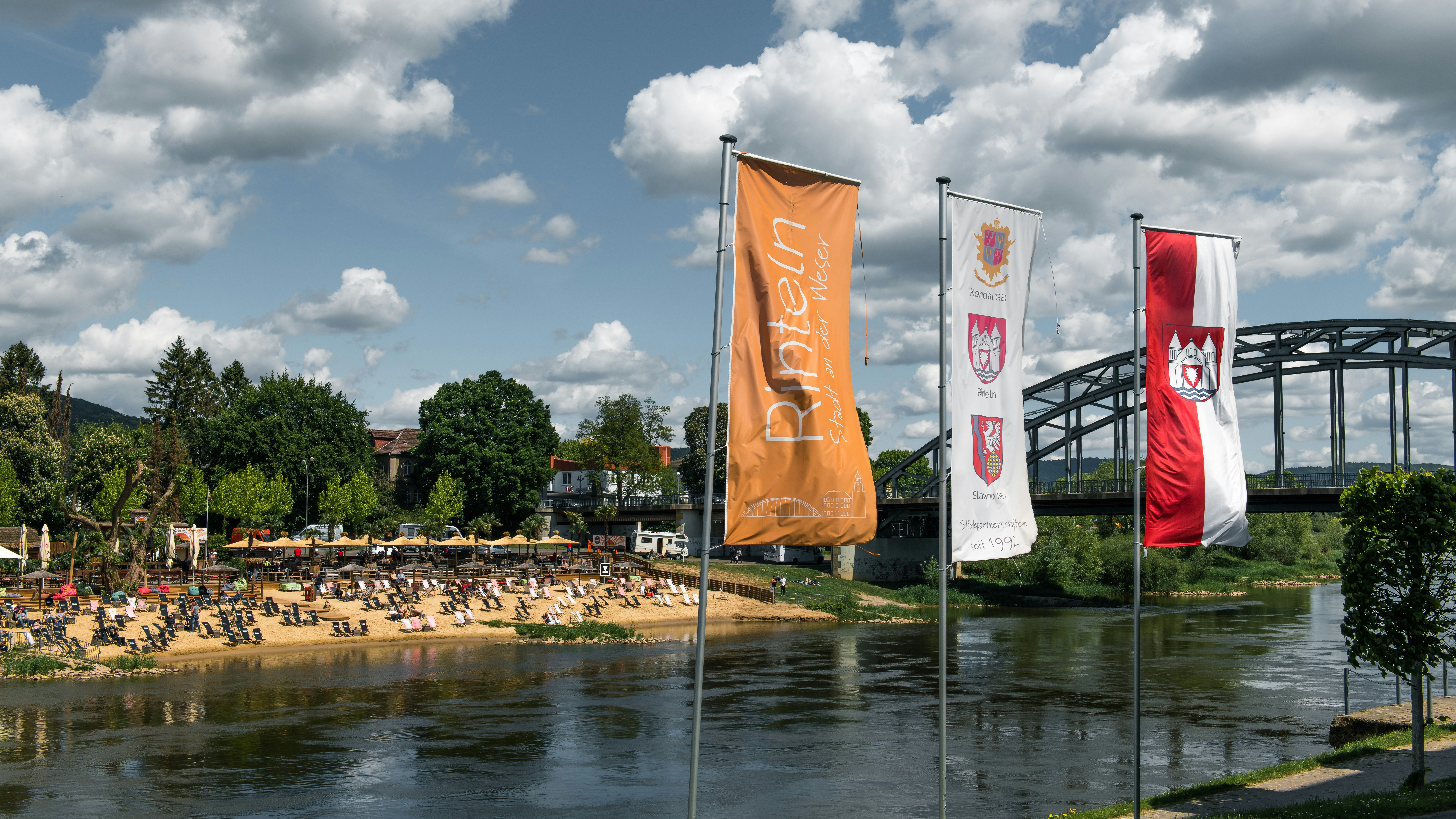 Flags fly over a river with a beach.