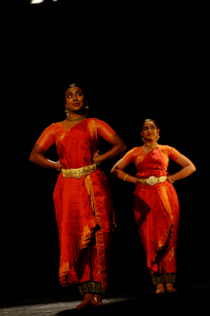 Two Bharatanatyam dancers in red costume performing a duet on stage